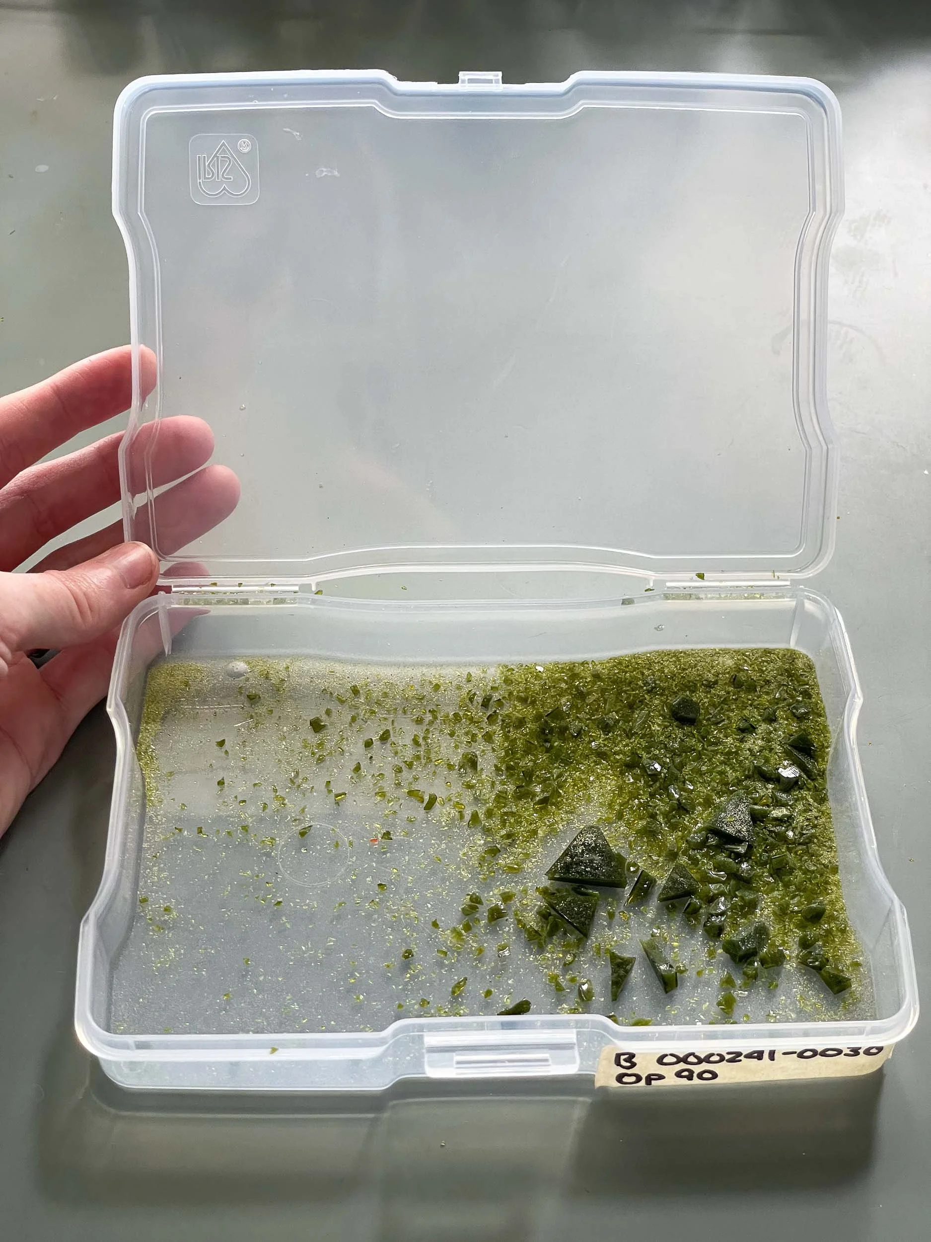 An open photo container filled with green stained glass scrap and frit