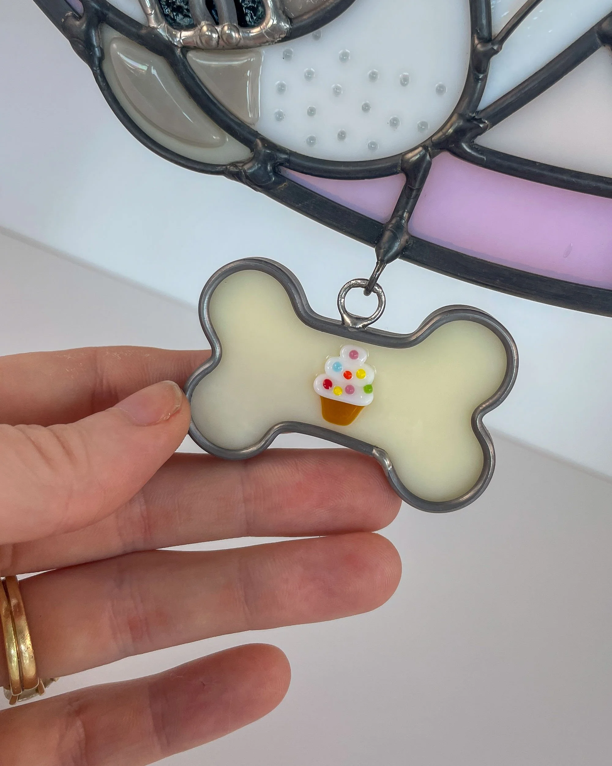 A closeup of a fused glass bone-shaped dog tag with a cupcake, attached to the pet portrait of a dog named Cupcake
