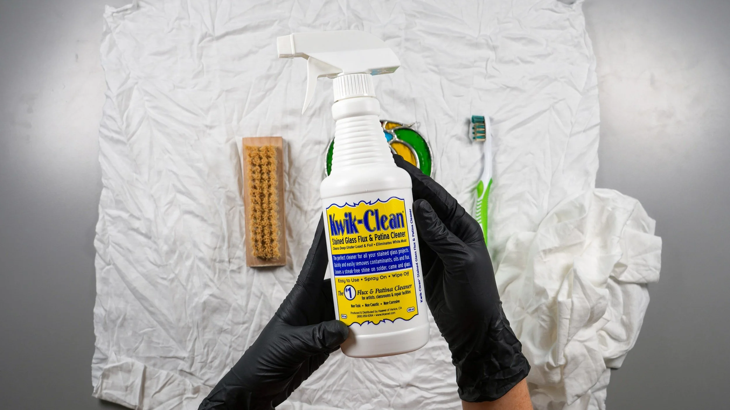 A bottle of Kwik-Clean held above a stained glass project on a clean cloth