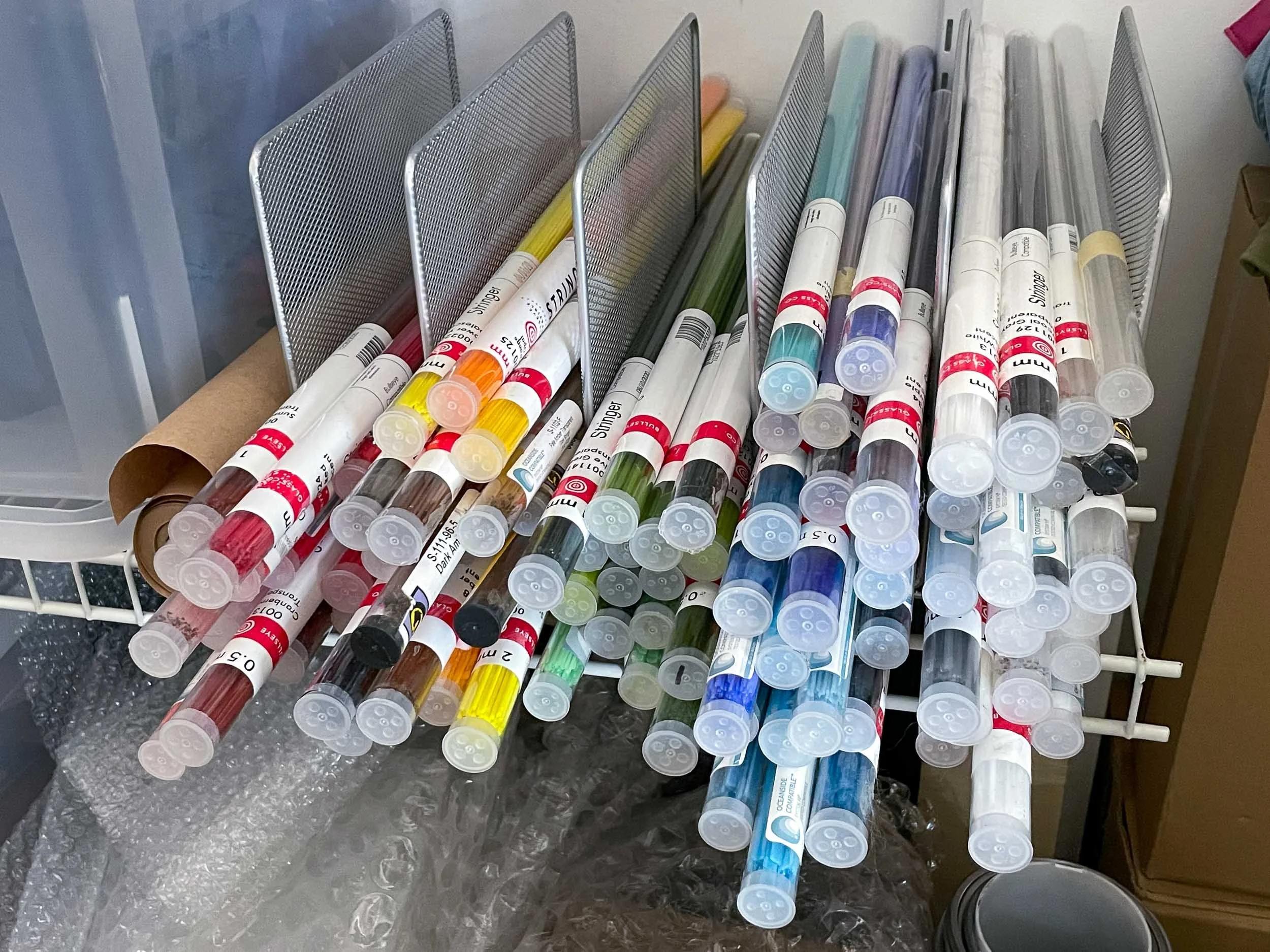 Various stained glass stringers and noodles arranged by color in a metal file organizer
