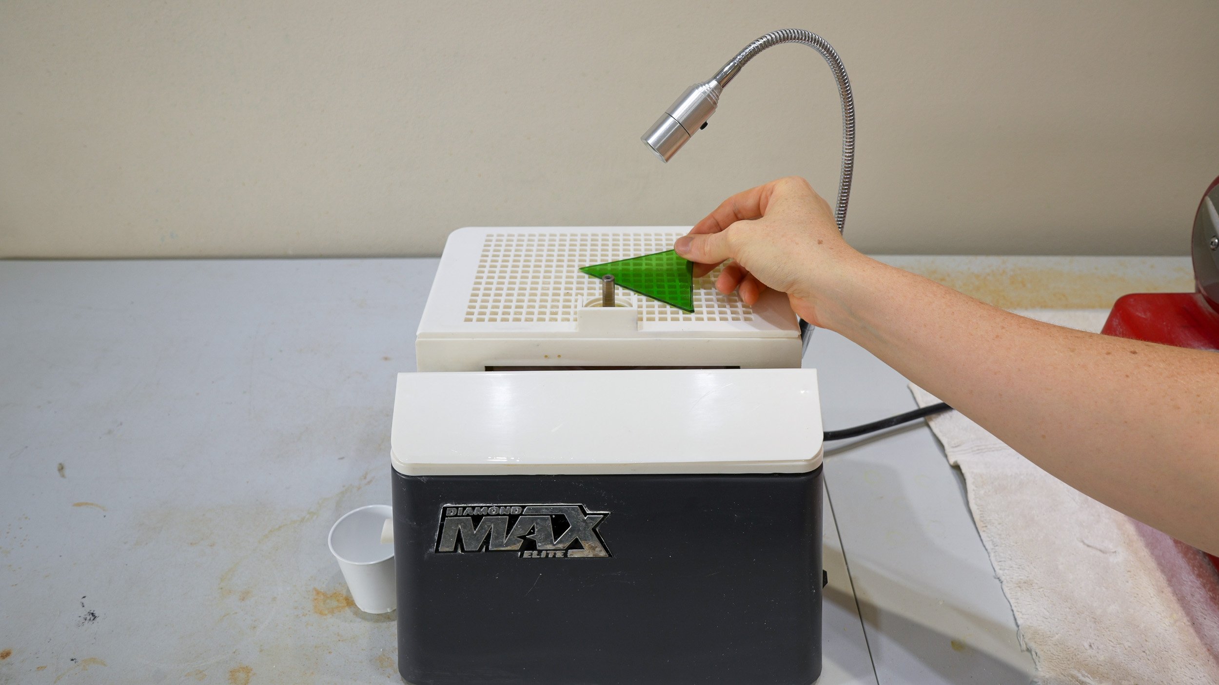 A straight-edged stained glass shape in front of an electric disc grinder