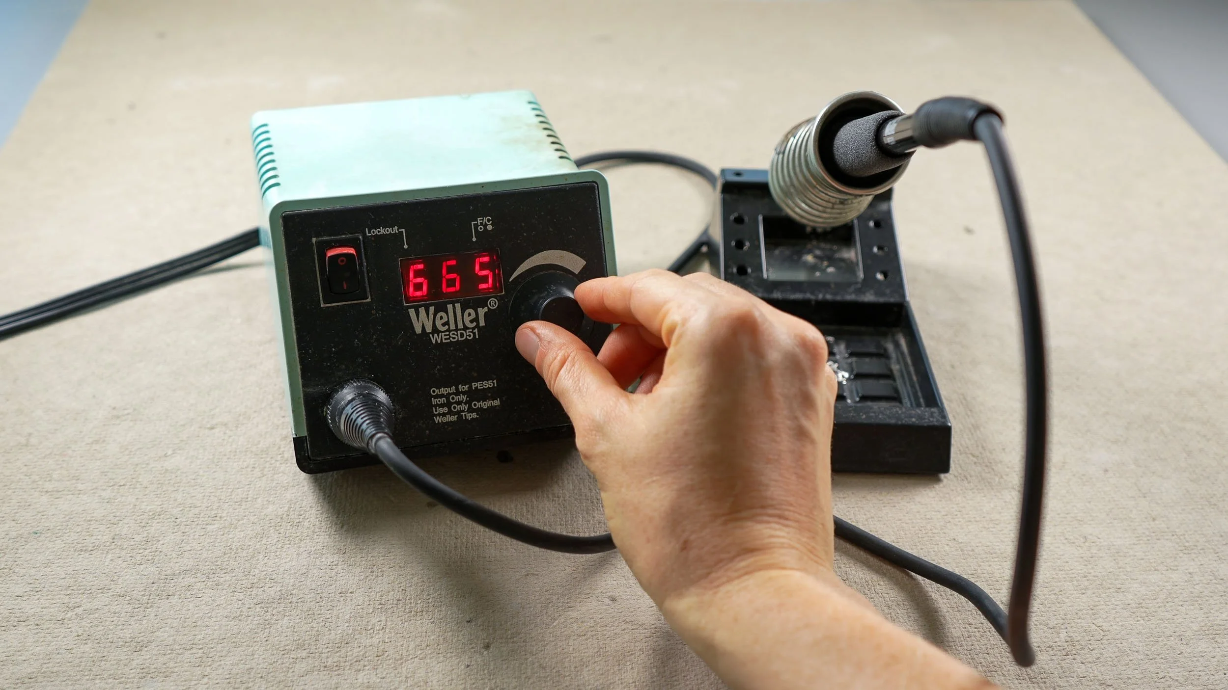 A hand adjusting the temperature dial of a stained glass soldering iron