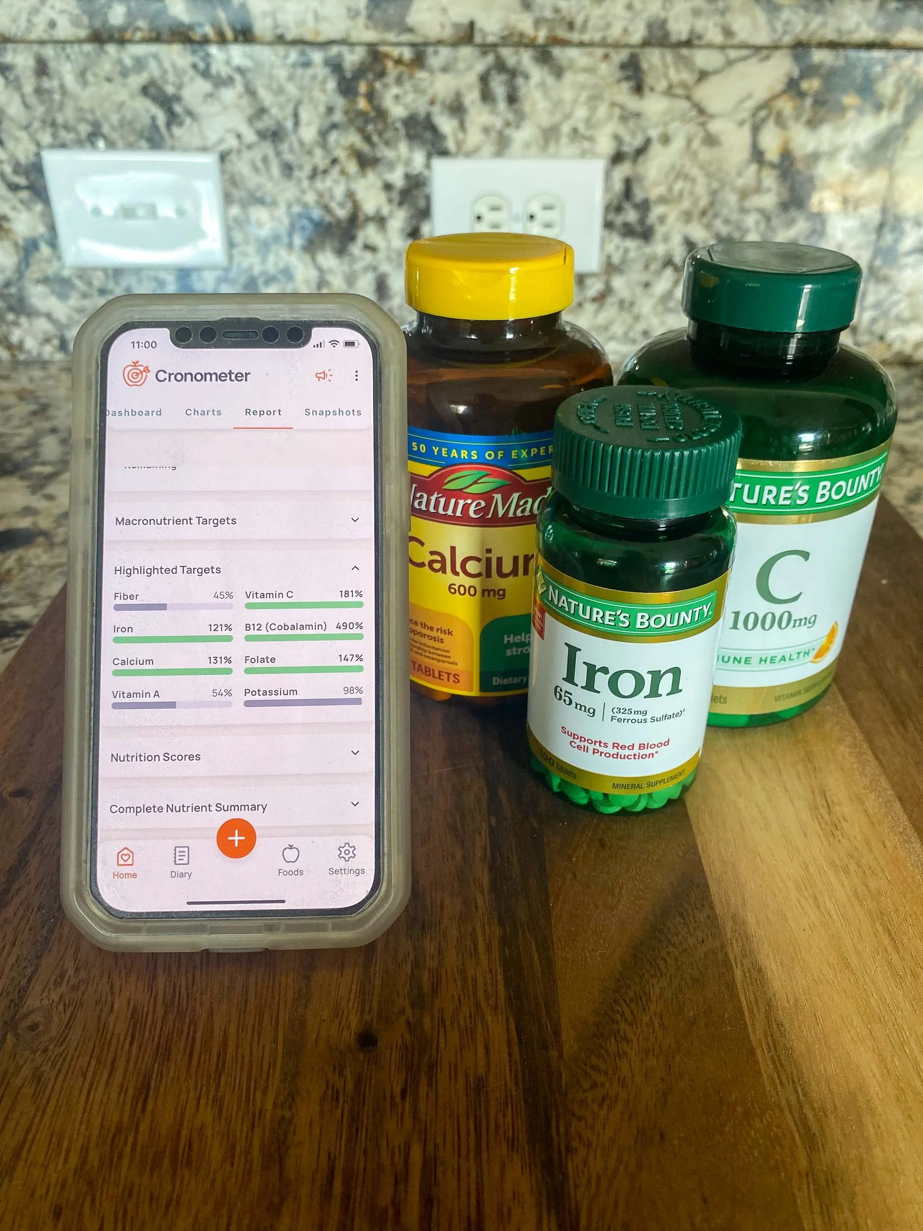 An iphone open to the Cronometer app, next to bottles of calcium, vitamin C, and iron