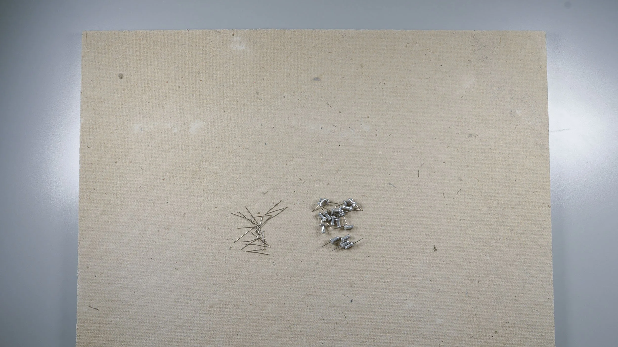 Piles of thumbtacks and dressmaker pins on a homasote insulation board
