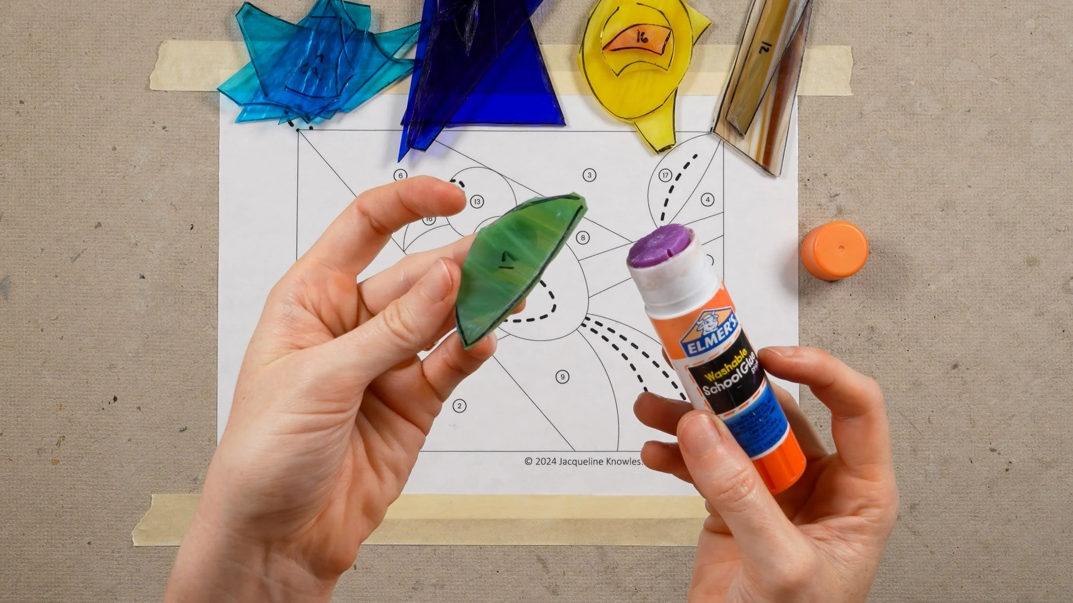 A glue stick being run over traced marker lines on a stained glass shape