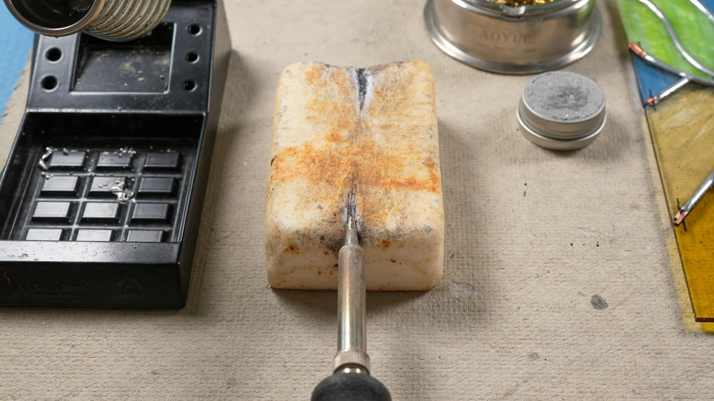A soldering iron tip being cleaned on a sal ammoniac block, next to a tin of paste tip tinner