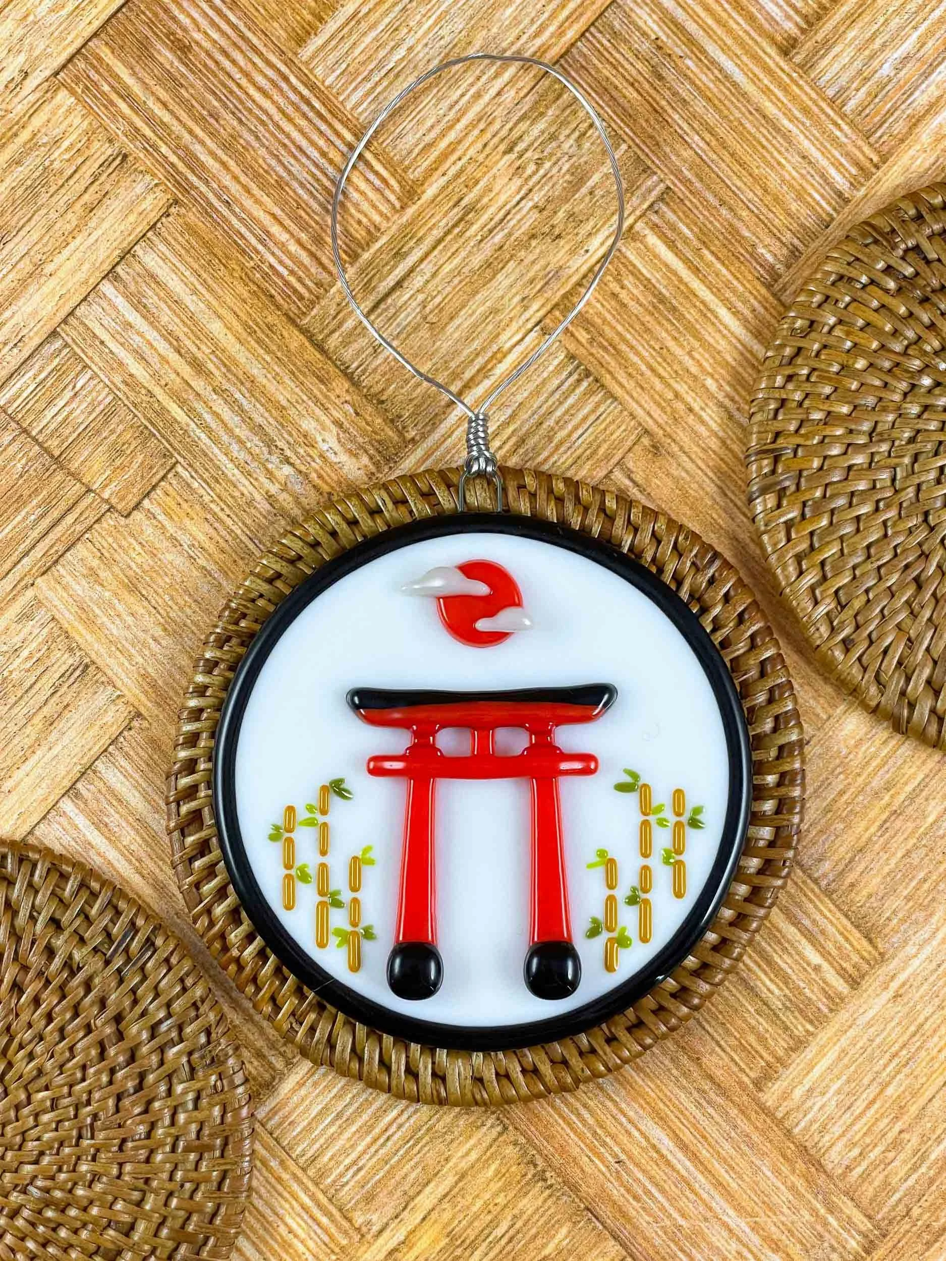 A fused glass ornament depicting a Japanese torii gate surrounded by bamboo