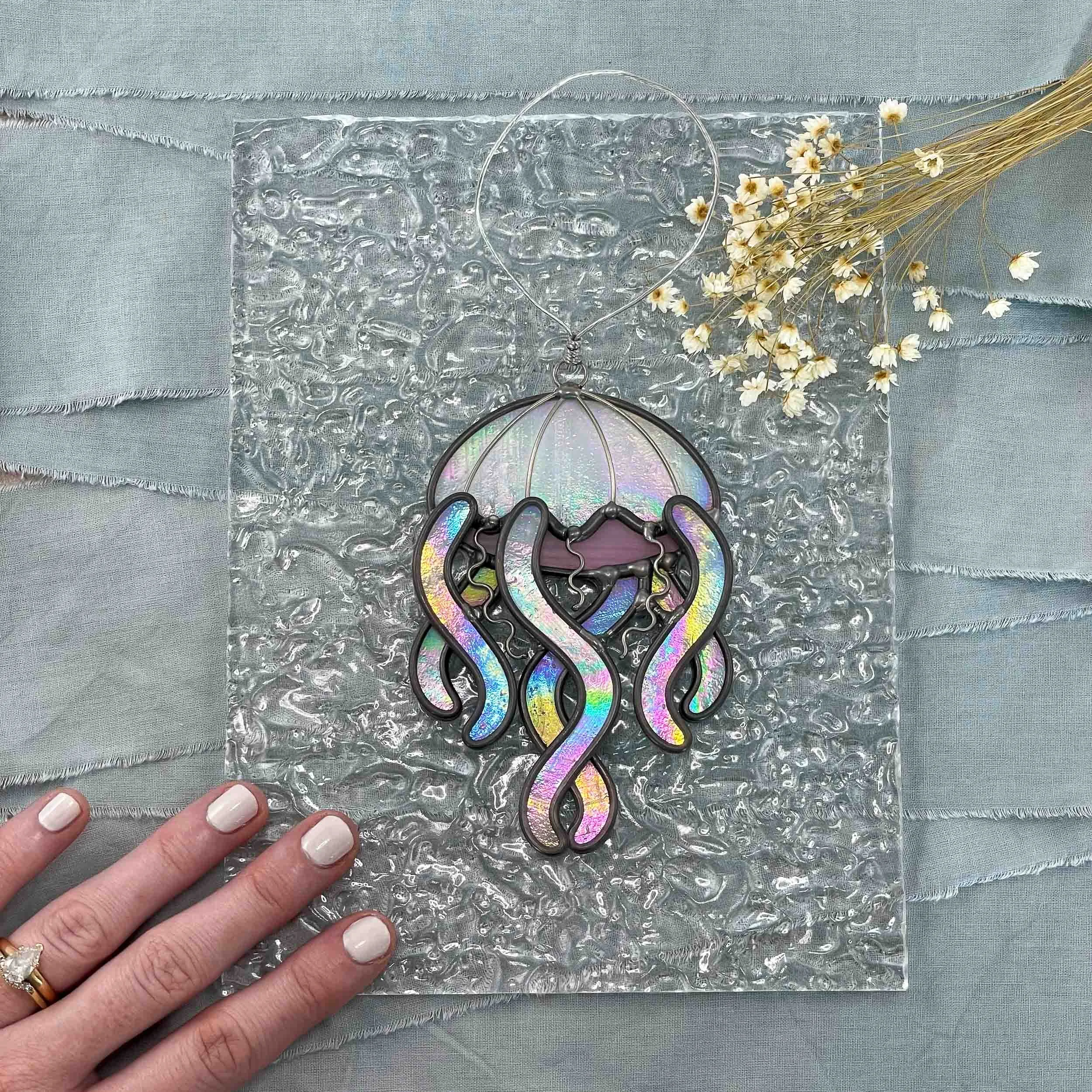 A vibrantly iridescent jellyfish ornament displayed next to small flowers