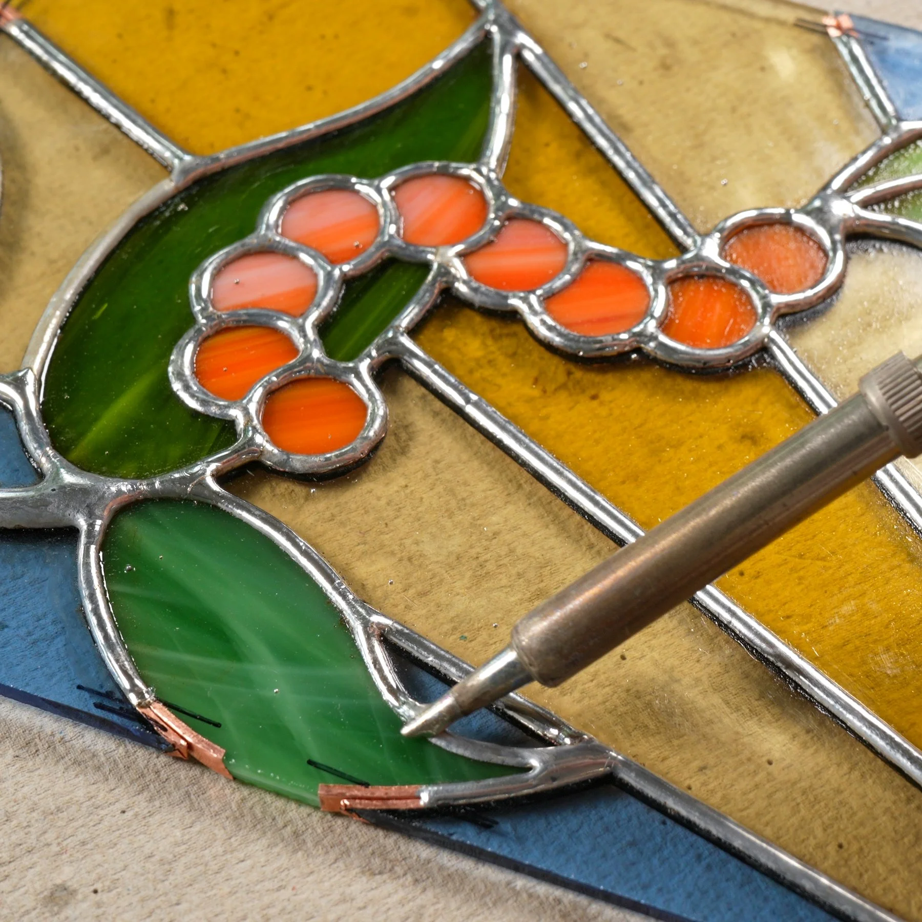 A soldering iron soldering the copper foil seam of a stained glass caterpillar project