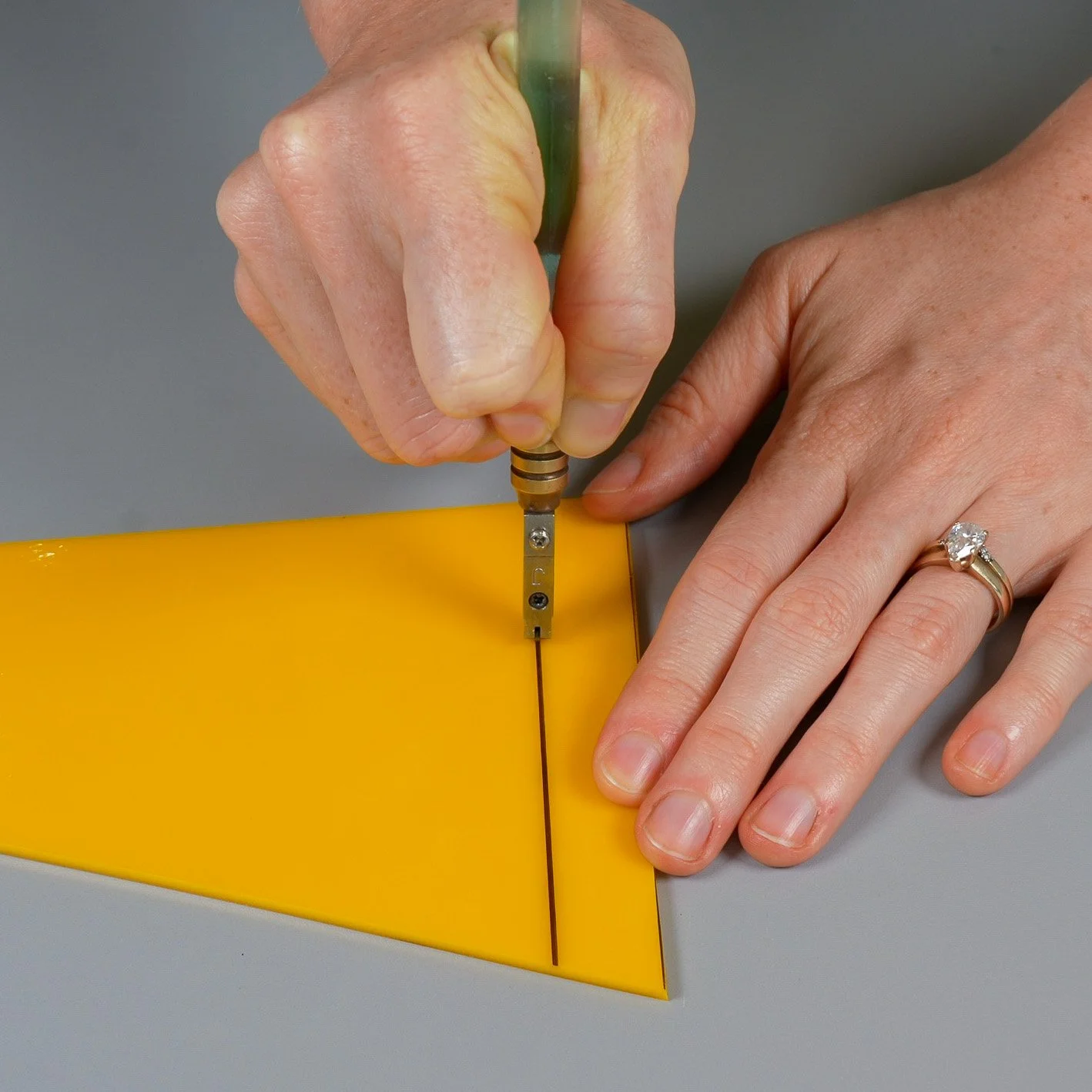 Glass cutter being used to score a straight line in a yellow stained glass sheet