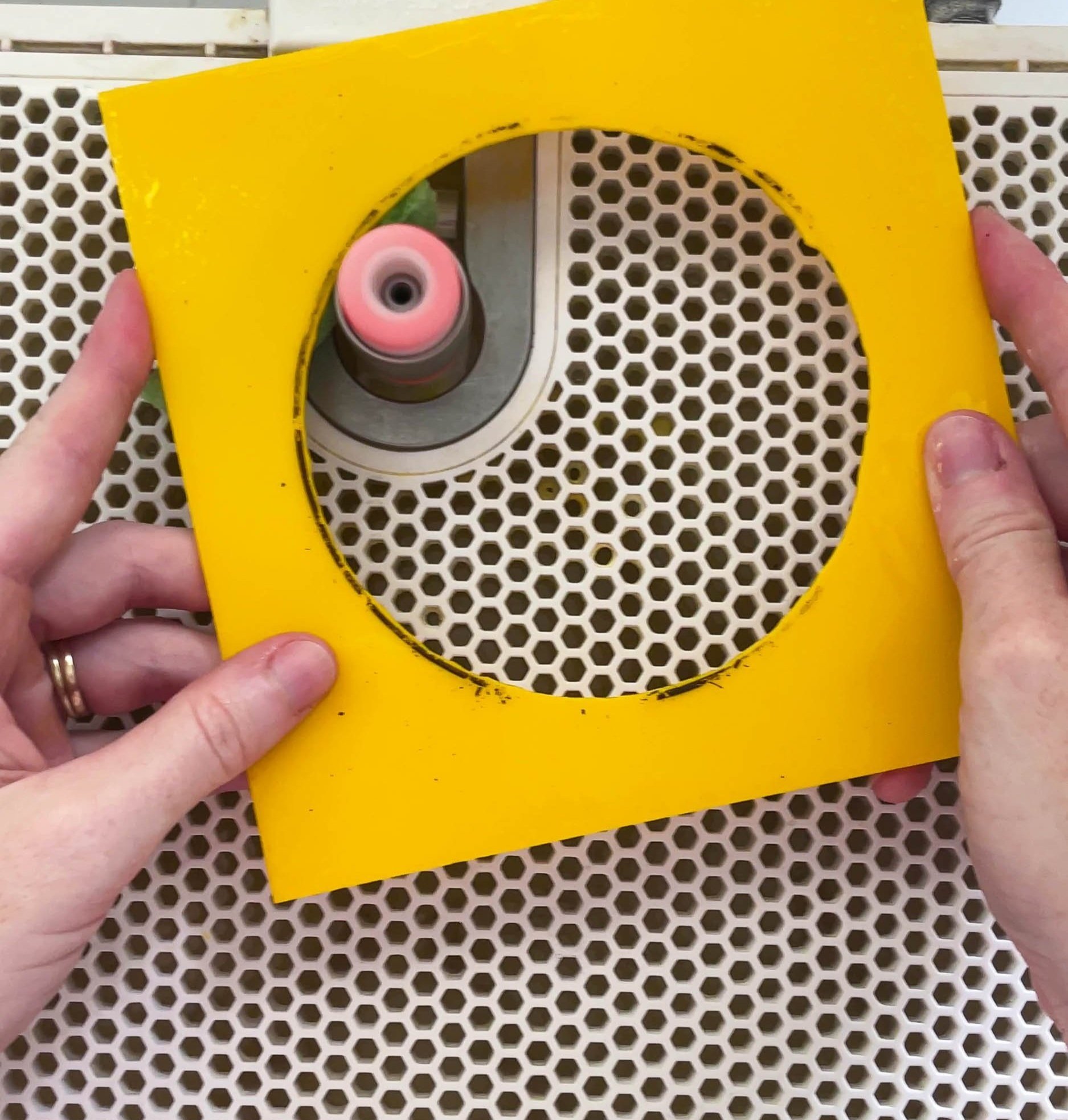Hands using an electric grinder to refine a perfectly circular cutout within a stained glass sheet
