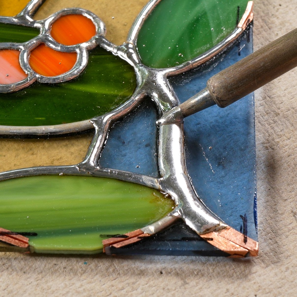 A soldering iron creating a thick solder bead in a stained glass project