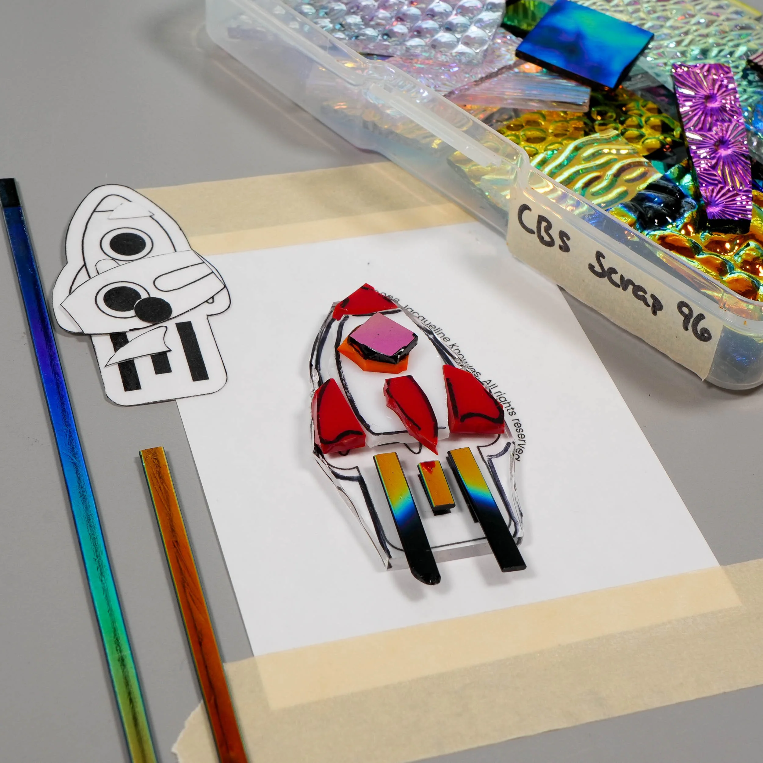 An in-progress fused glass rocketship pin made with dichroic sheet glass and noodles