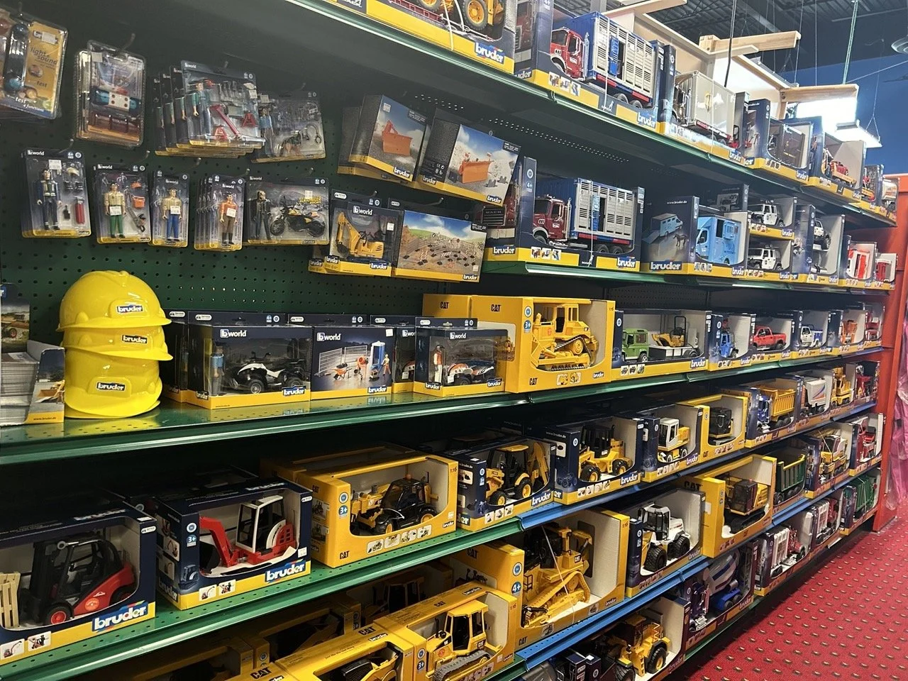 A store shelf filled with toy construction vehicles, trucks, and accessories, including yellow hard hats.