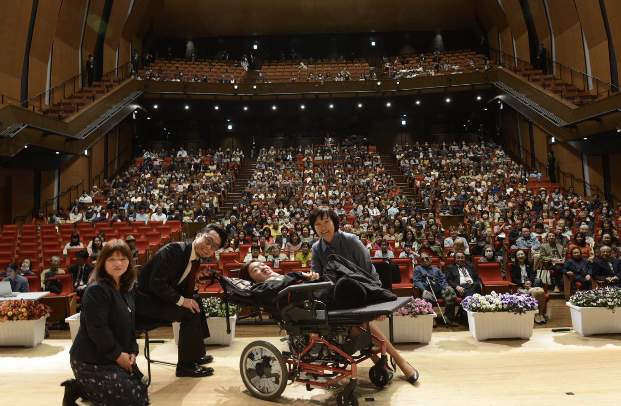 Hisamu-san in front of a crowd, in an auditorium 