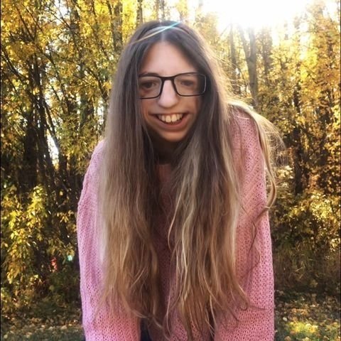  Anah smiling and wearing glasses and a pink sweater.  