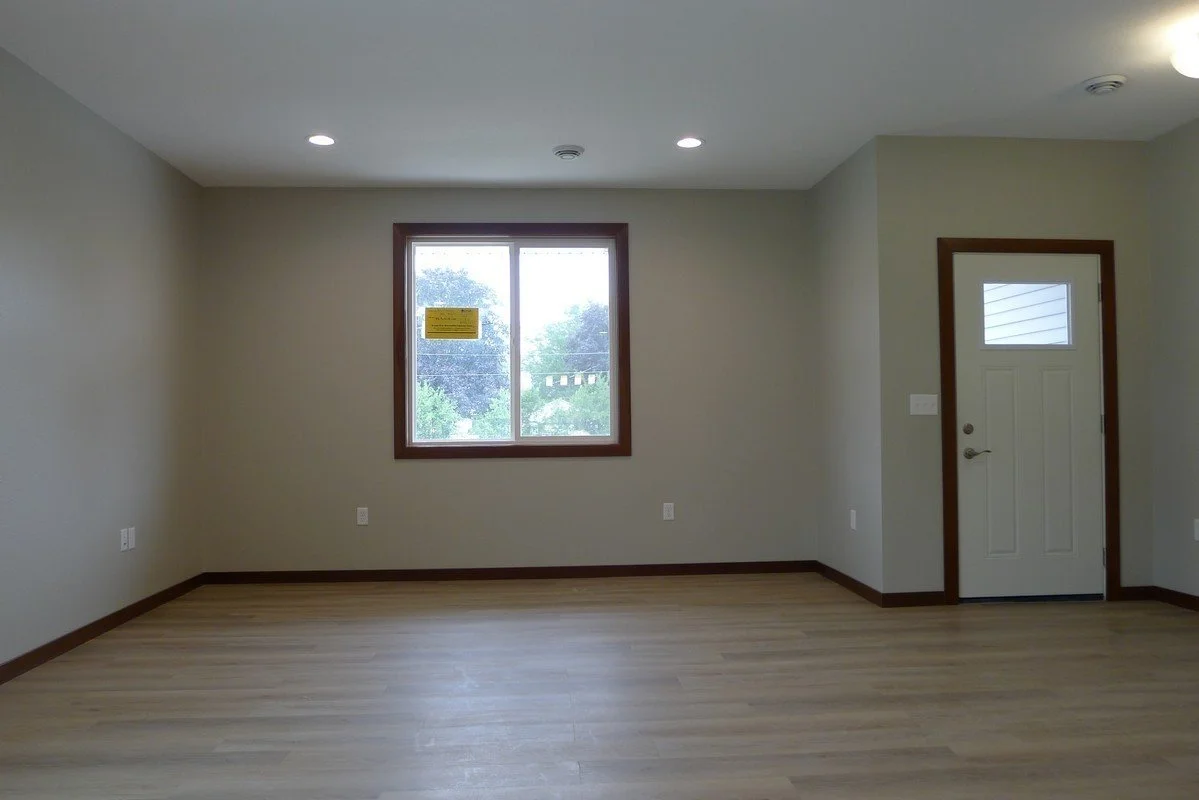 Empty room with beige walls, wooden floors, a window, and a white door with a small window.