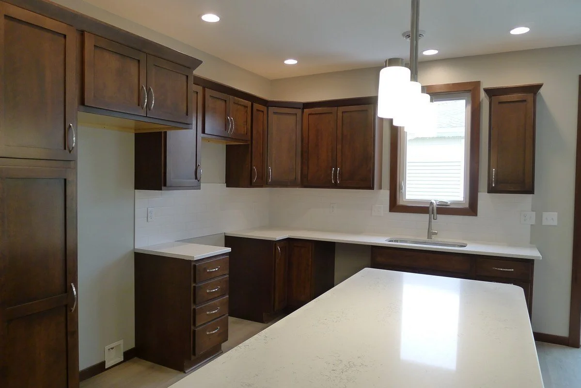 Kitchen with dark wood cabinets, white countertops, a window above the sink, and a hanging light fixture.