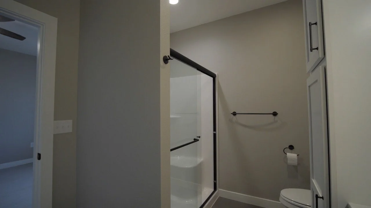 Bathroom with a shower enclosure with a glass door, white bathtub, toilet, and tall white cabinet.