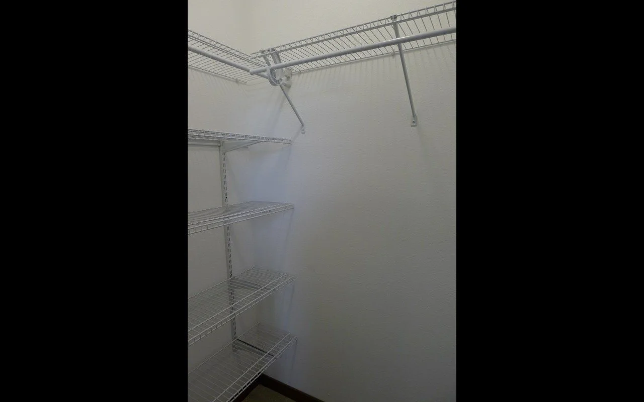 Empty closet with white wire shelving and a horizontal clothing rod.