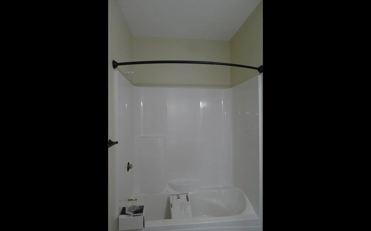 Empty bathtub shower combo with a curved shower curtain rod in a bathroom with green walls.