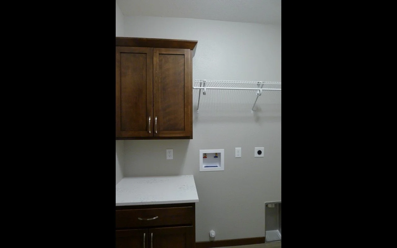 Empty laundry room with wooden cabinets, a white countertop, a wire shelf, and wall hookups for a washer and dryer.