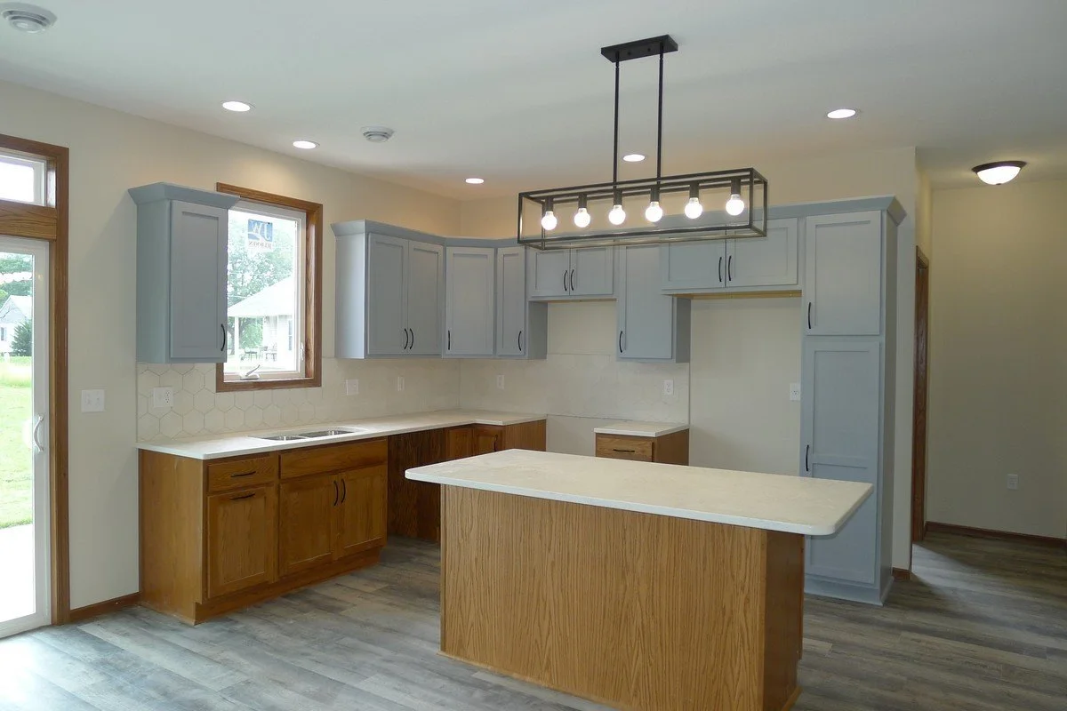 Kitchen with gray and wooden cabinets, a white countertop island, and a modern rectangular light fixture with exposed bulbs hanging from the ceiling.