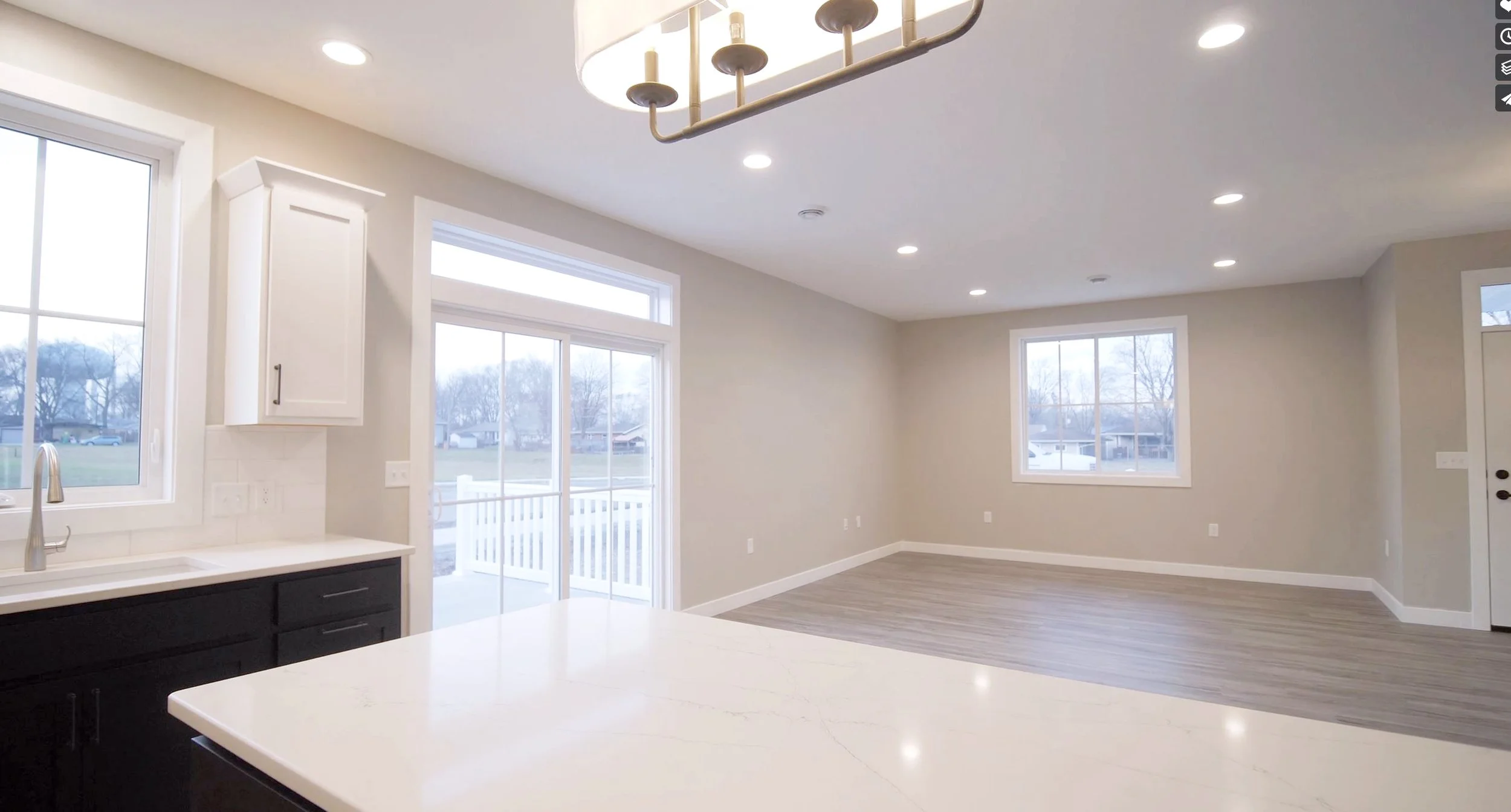 Empty open-concept living area and kitchen with large windows, hardwood floors, and recessed lighting in a modern home.
