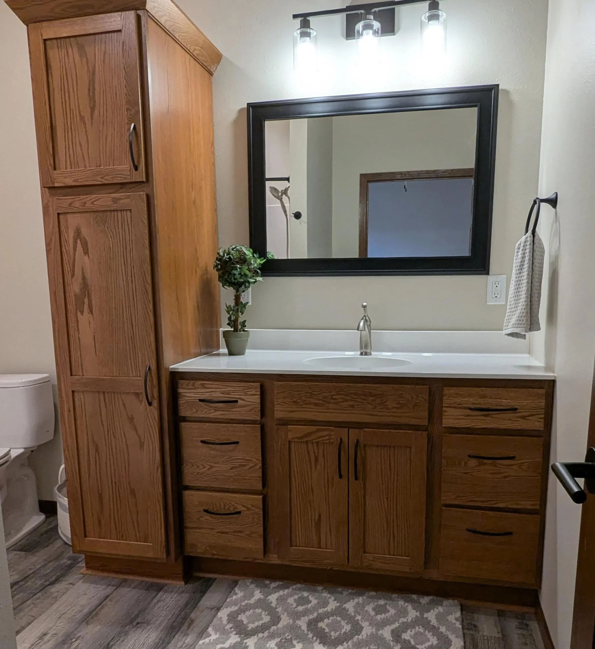 Bathroom vanity with a large mirror, wooden cabinet, potted plant, and a towel hanging on a hook.