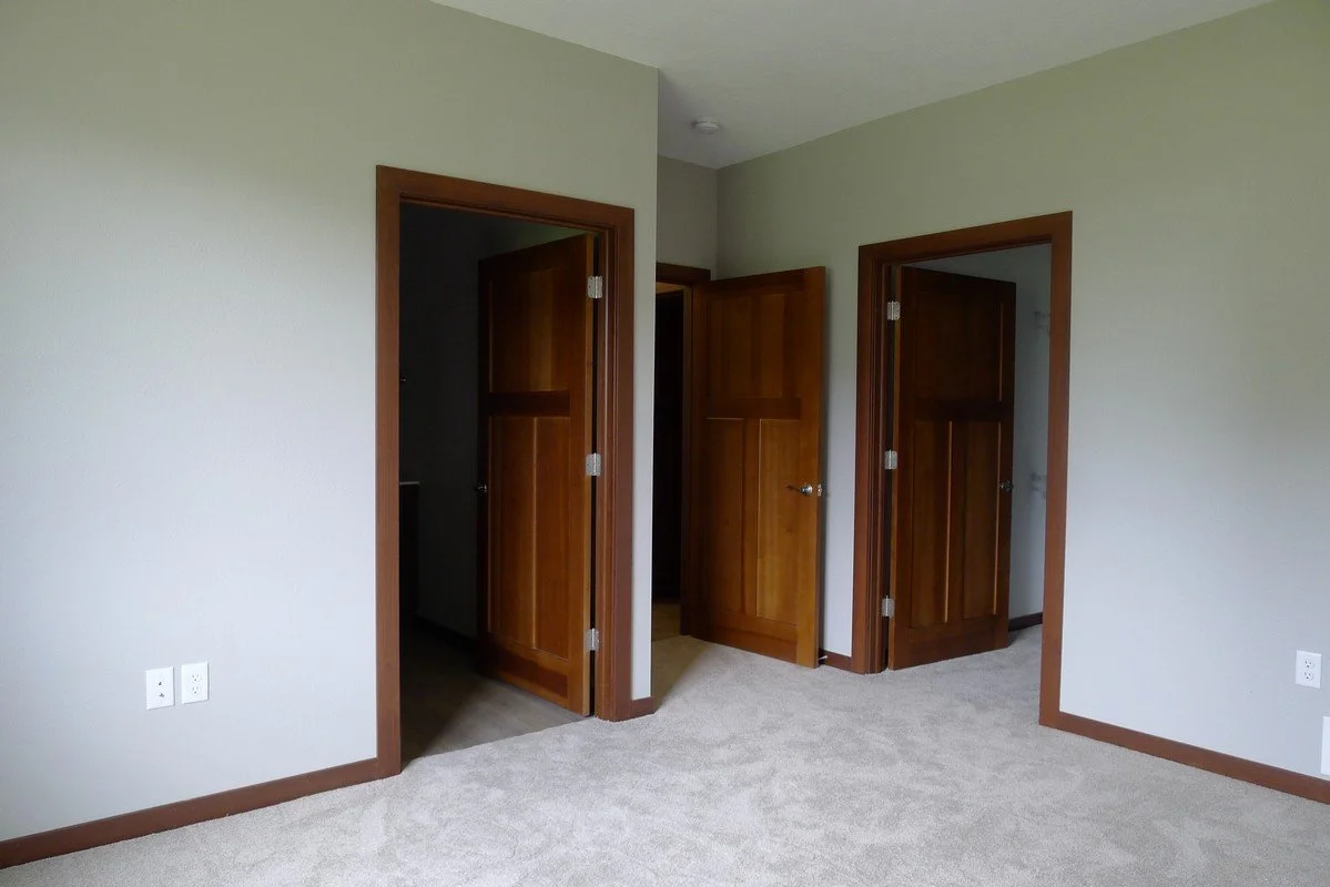 Empty room with three open wooden doors, light-colored walls, and beige carpet.