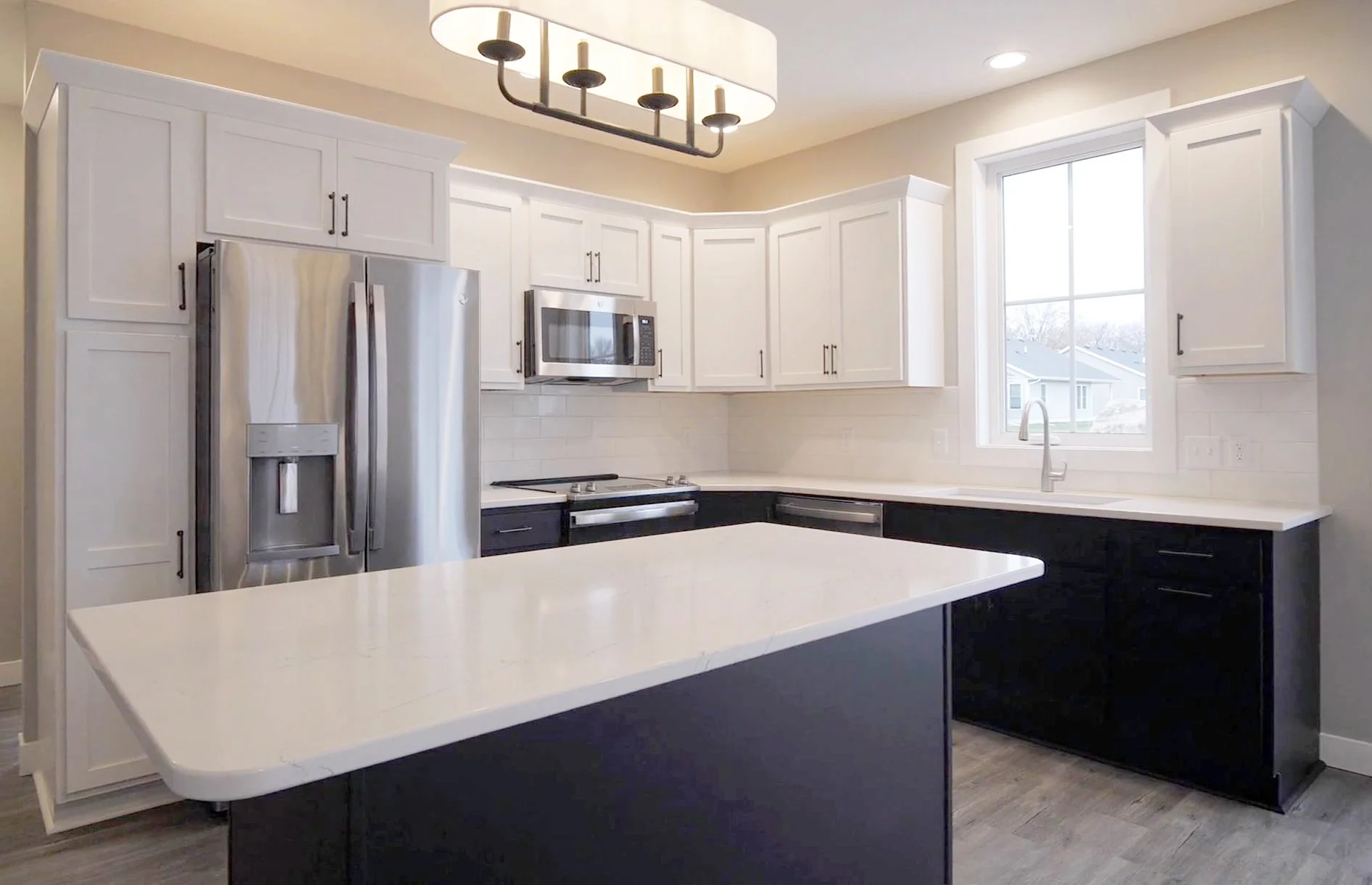 Modern kitchen with white upper cabinets, black lower cabinets, stainless steel appliances, a large window, and a kitchen island.