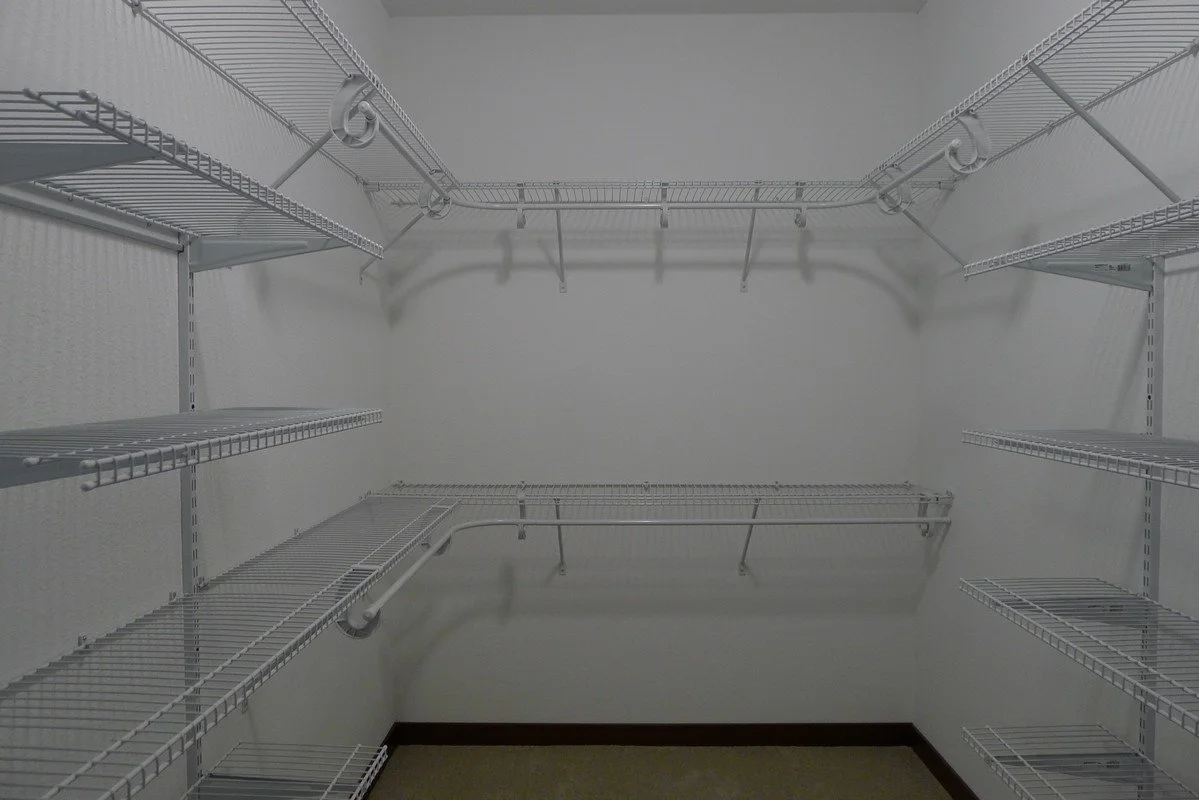 Empty walk-in closet with white wire shelving units on three walls and a beige carpeted floor.