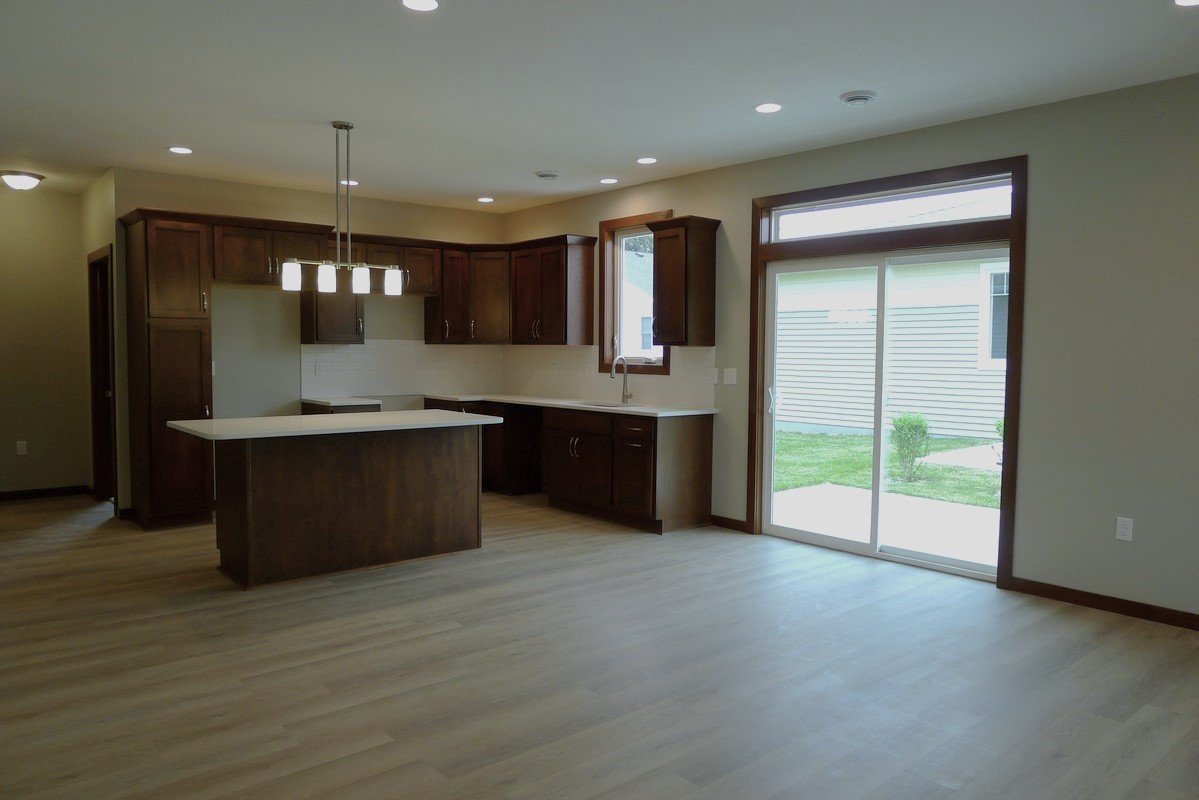Empty kitchen and dining area in a modern home with wooden cabinets, a sliding glass door, and a light-colored floor.
