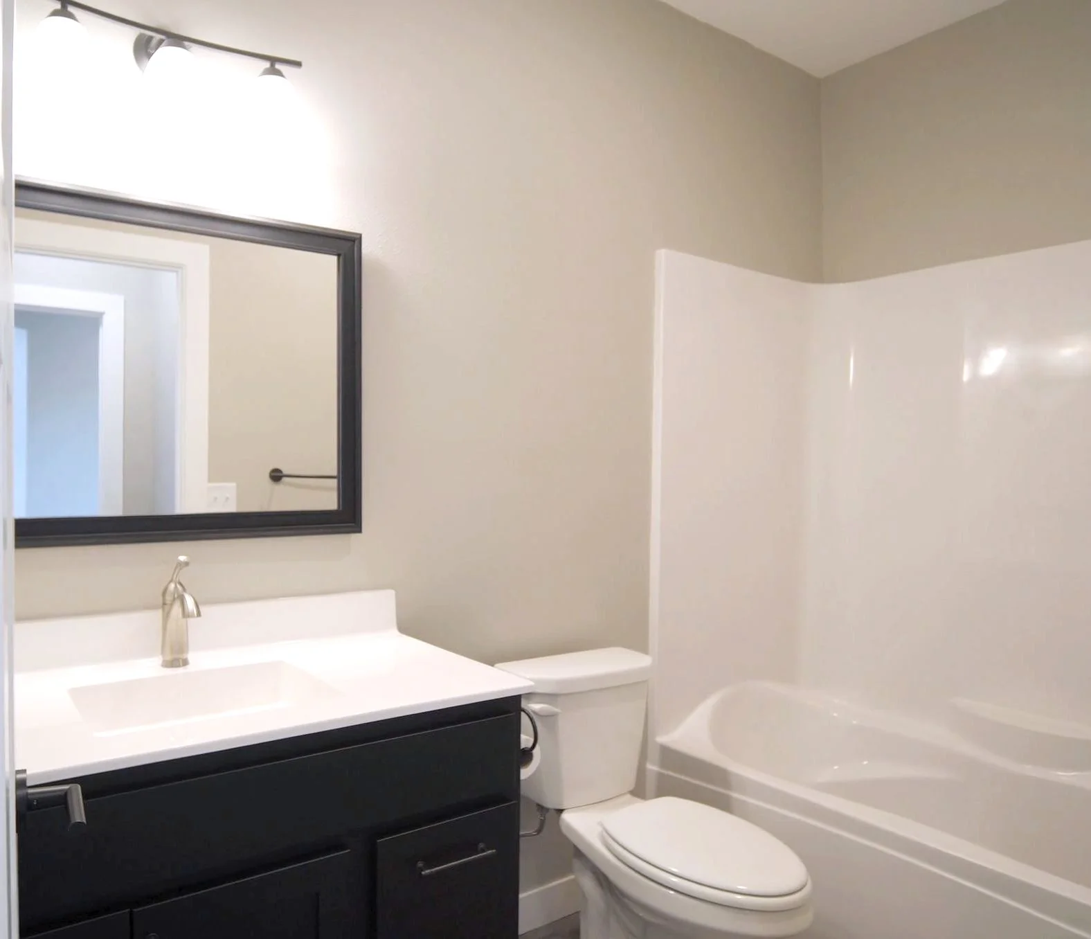Modern bathroom with a white bathtub, toilet, black vanity with a white countertop, and a mirror above the sink.