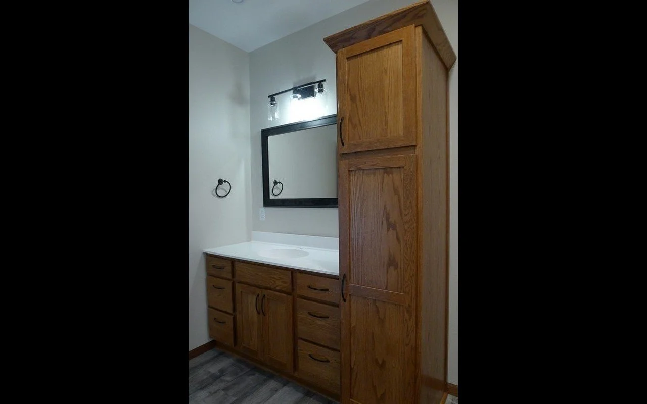 Bathroom vanity with wooden cabinets, a mirror, and a black light fixture.