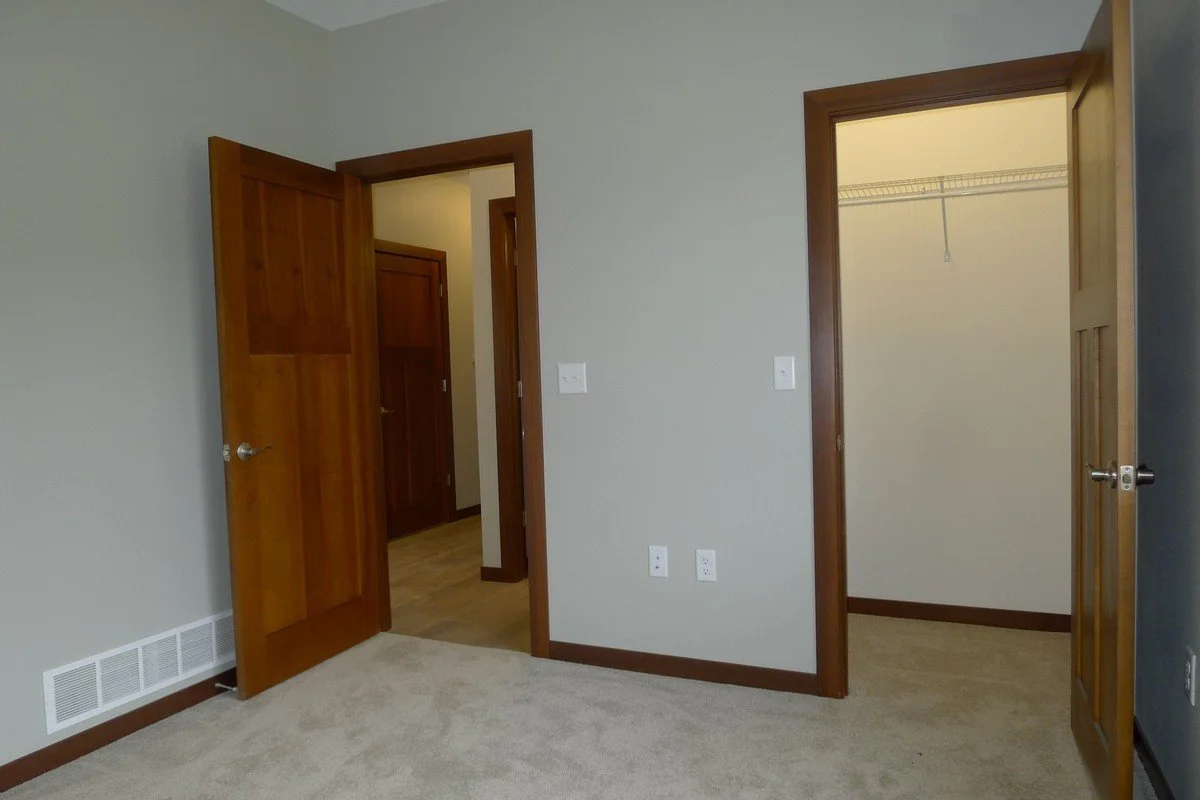 Empty room with beige carpet, light gray walls, two open wooden doors leading to closets or rooms, and a vent near the floor.