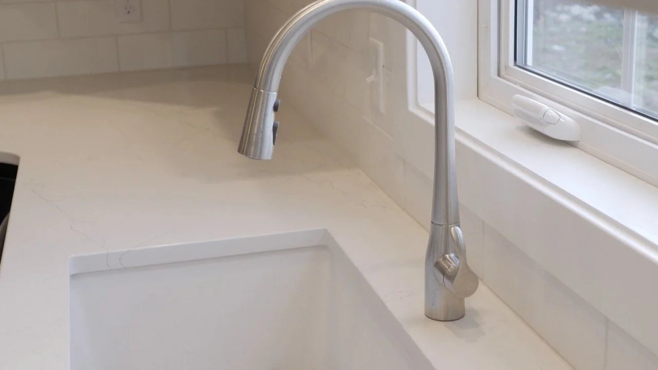 A kitchen window above a white marble countertop with an undermount sink and a modern stainless steel faucet.
