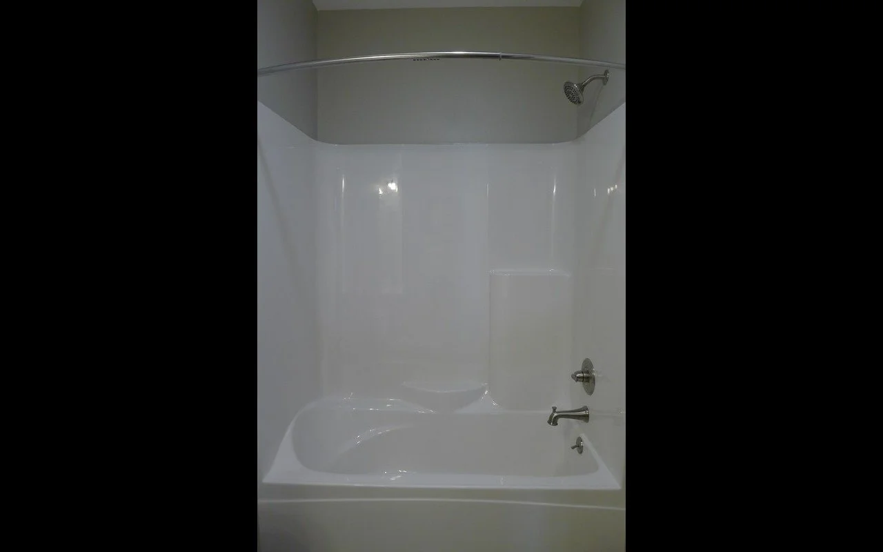 Empty white bathtub with shower faucet and showerhead in a bathroom.