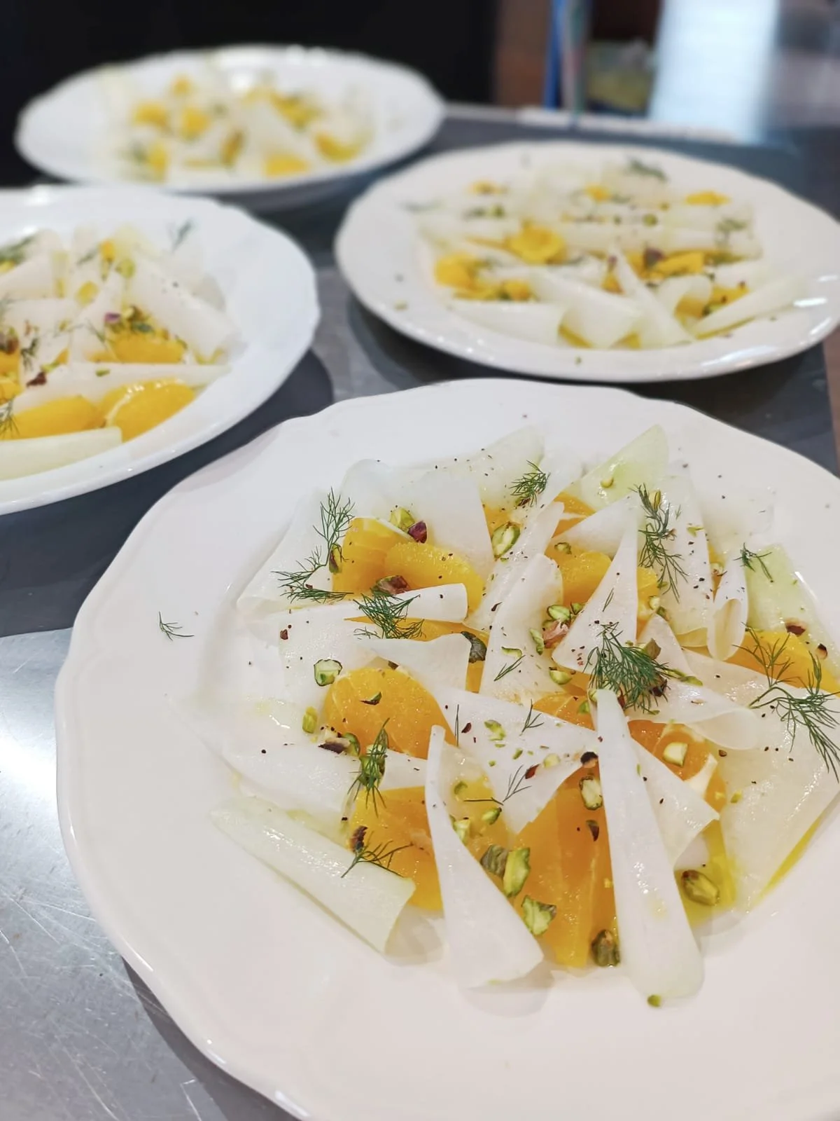 Salad with sliced fennel, orange segments, chopped pistachios, and fresh herbs on a white plate.