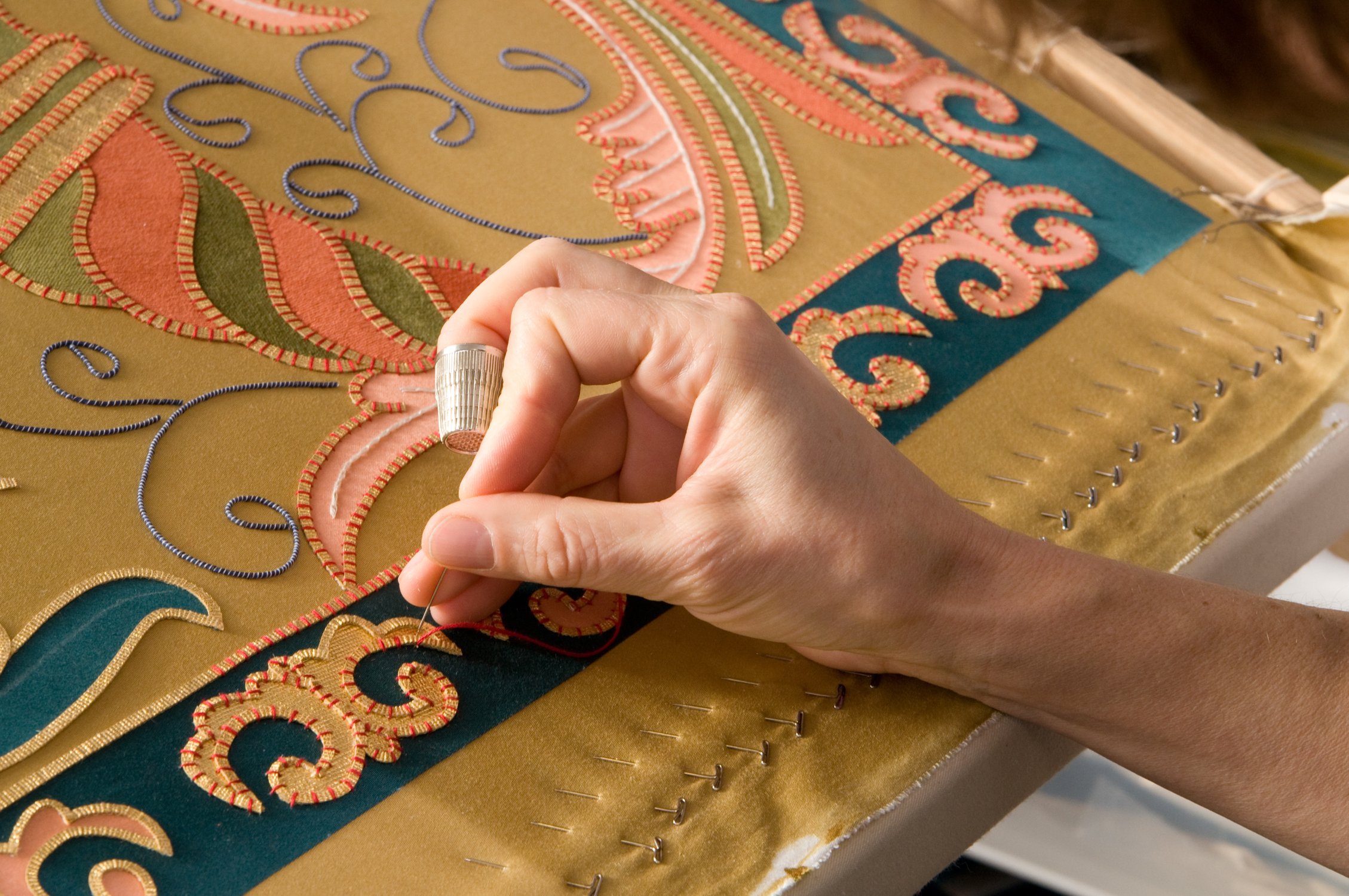 Using a thimble to couch down the 24kt gilded ribbon edging.