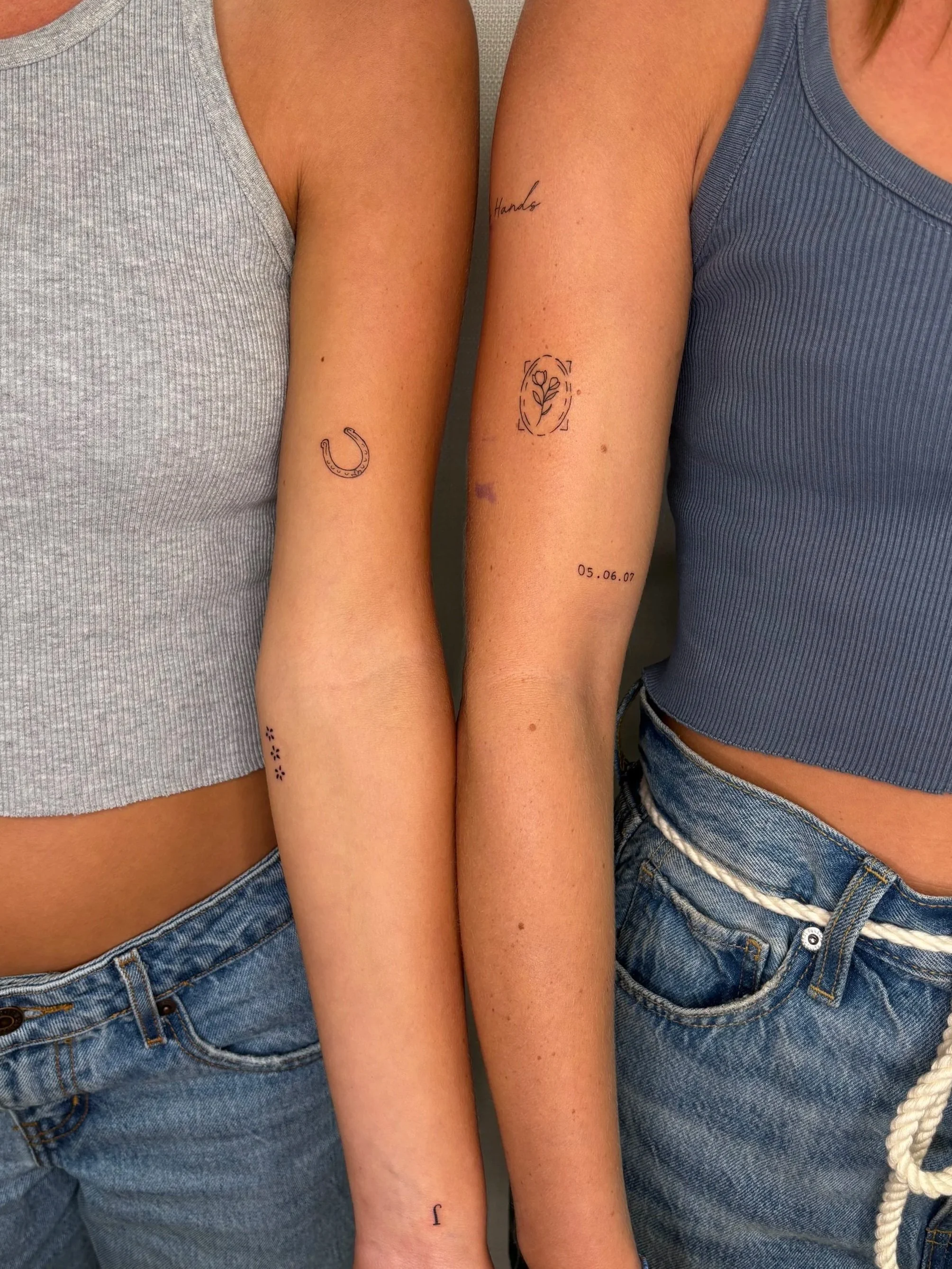Two people, one with a horseshoe tattoo and one with a flower tattoo both done by Brooke Kalynn