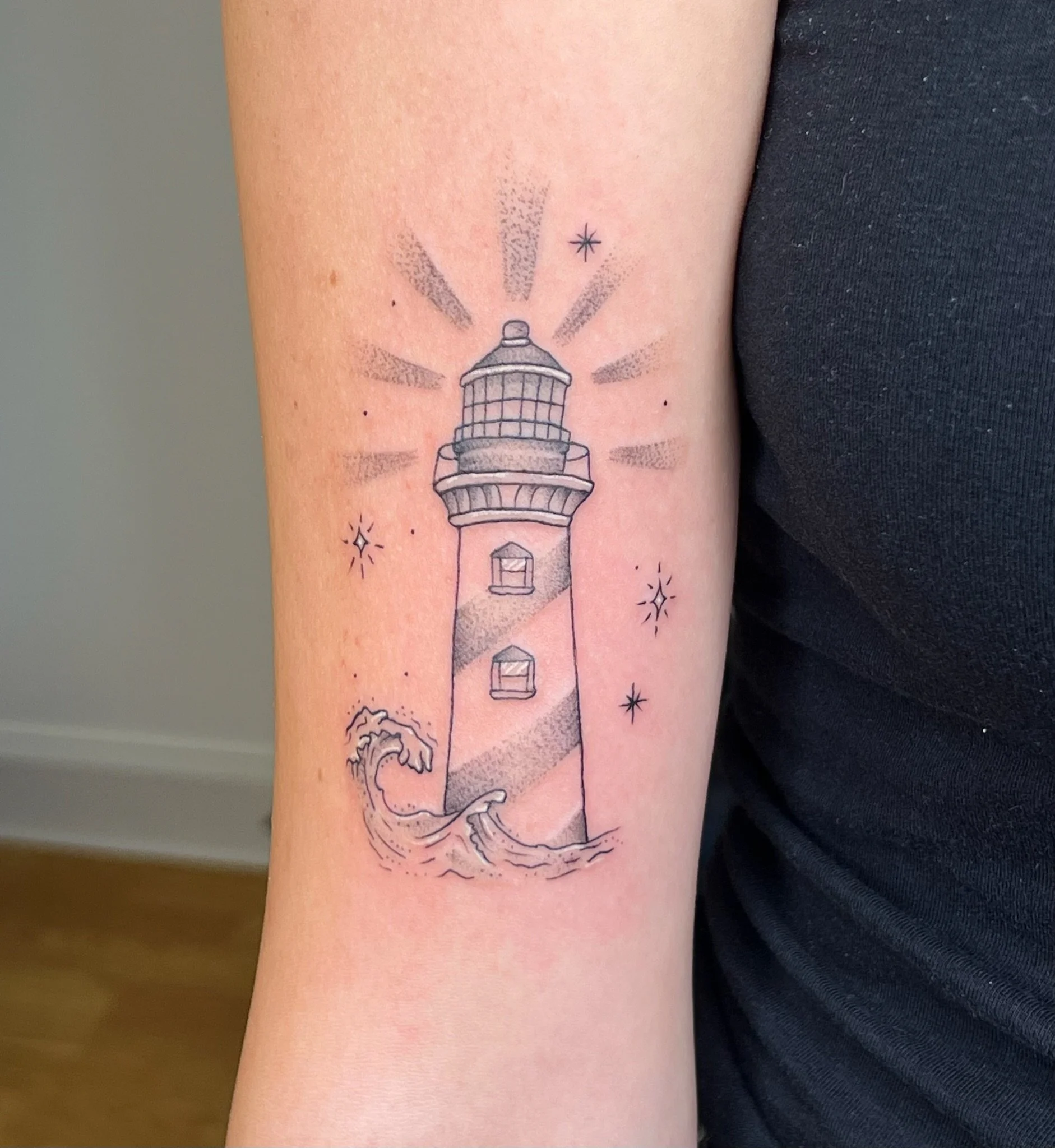 A lighthouse tattoo with light beams, stars and waves