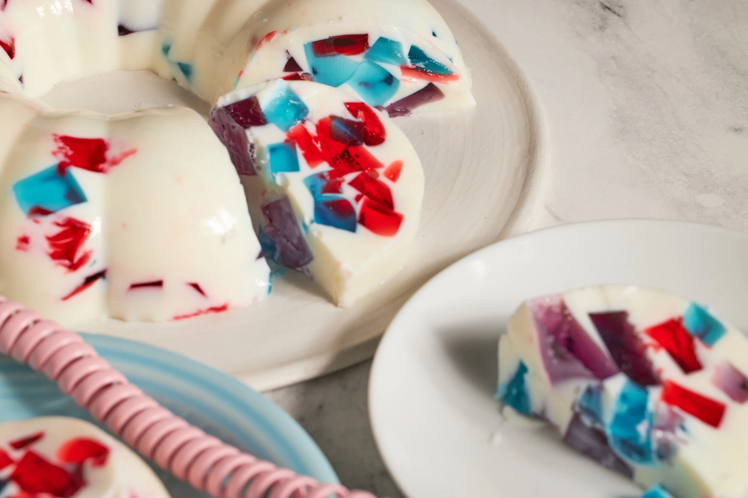 broken glass jello dessert purple pink and blue in a bundt cake shape on a neutral backdrop with bright on white plates jessica furniss