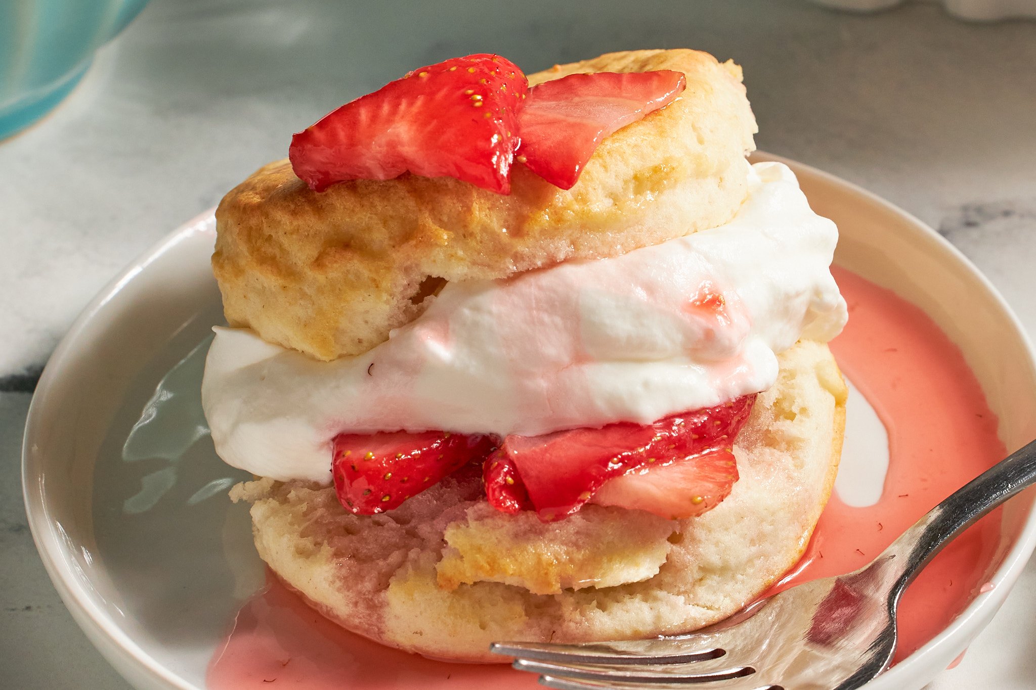 strawberry shortcake with biscuits fresh strawberries and whipped cream on a white plate with a fork on neutral background and aqua dishes