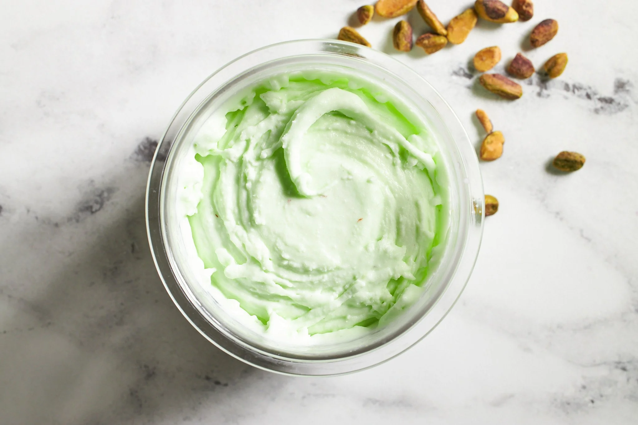 Pistachio ice cream from Ninja Creami in container on neutral surface with pistachios in the background