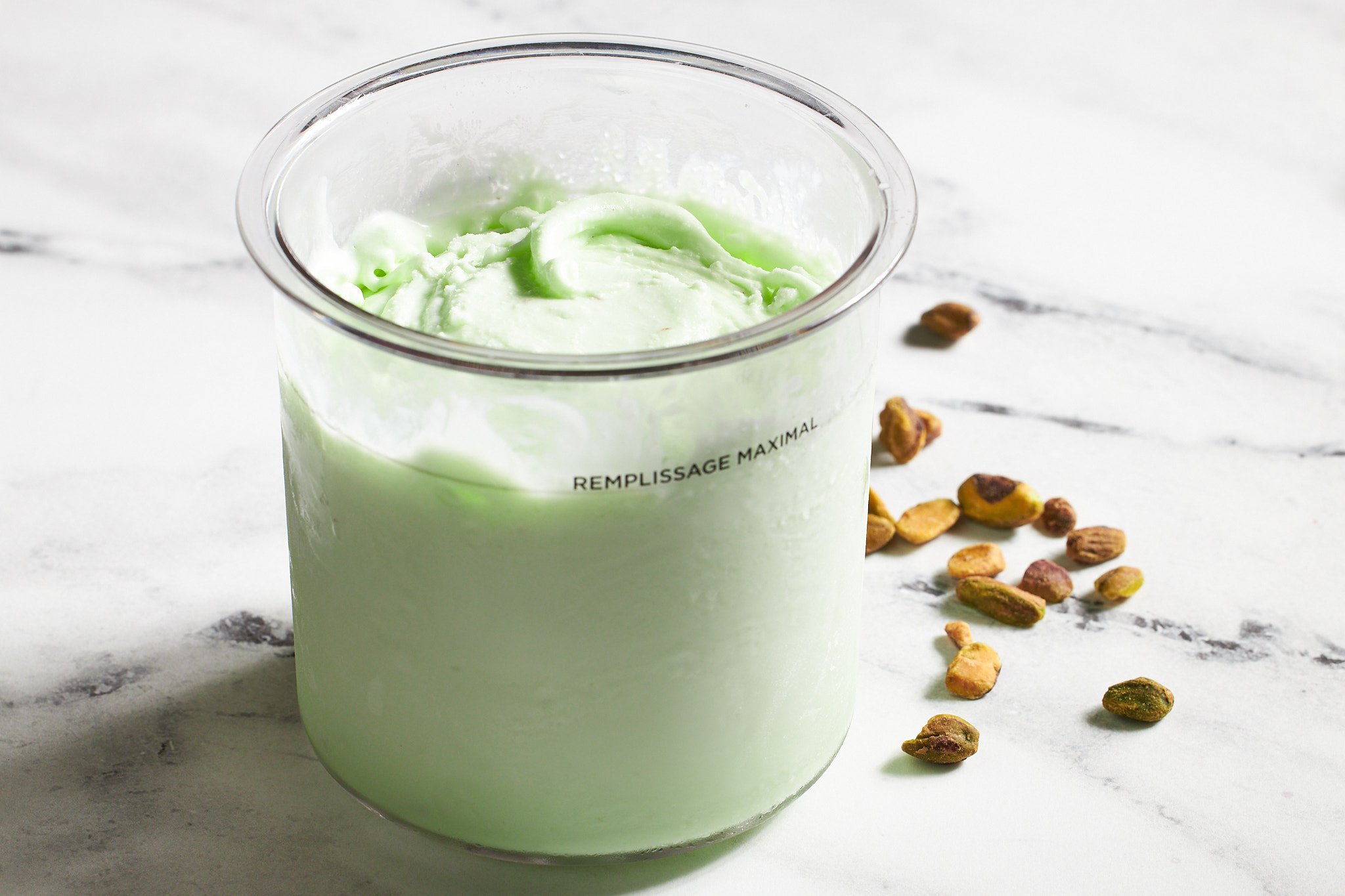 Pistachio ice cream from Ninja Creami in container on neutral surface with pistachios in the background