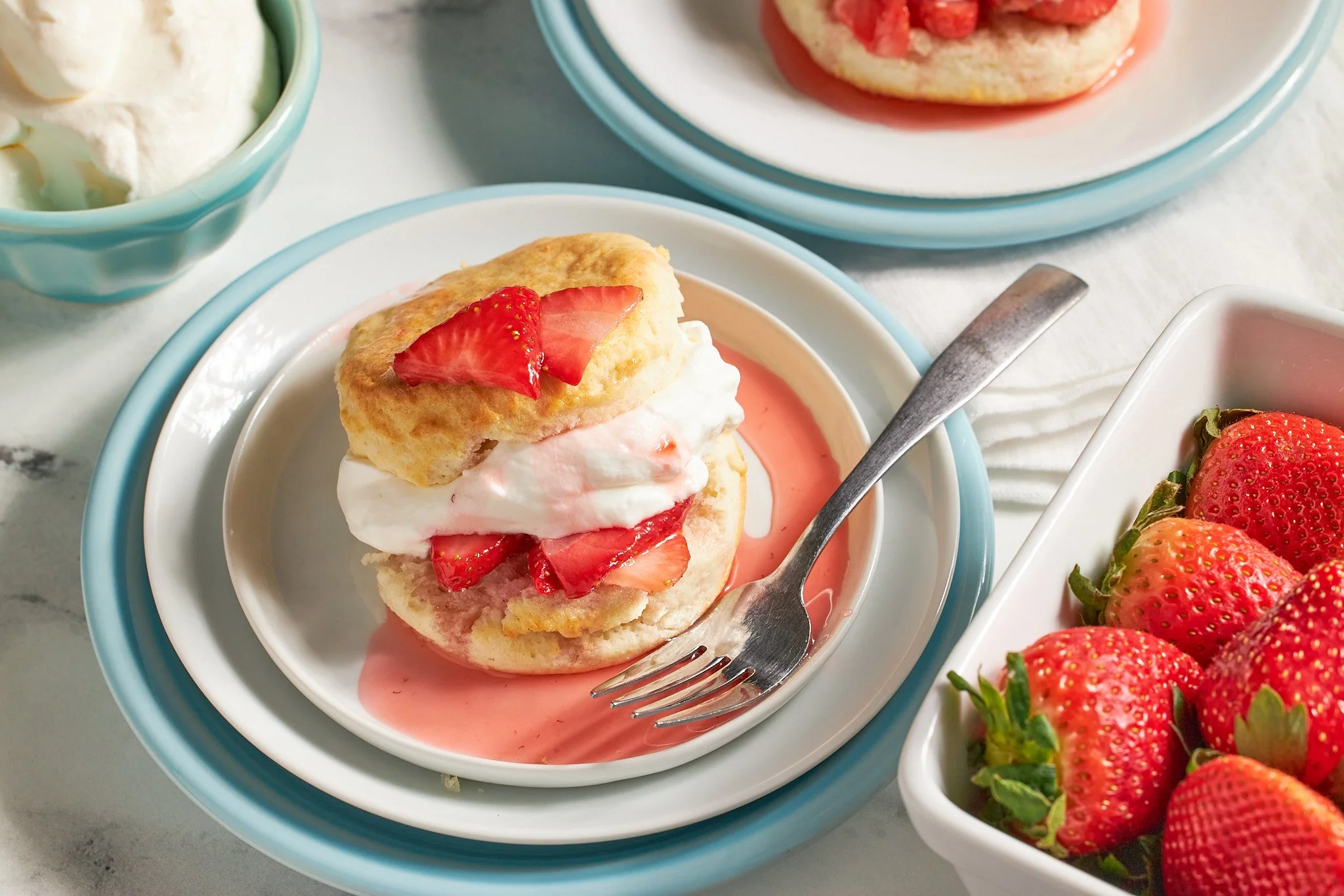 strawberry shortcake with biscuits fresh strawberries and whipped cream on a white plate with a fork on neutral background and aqua dishes