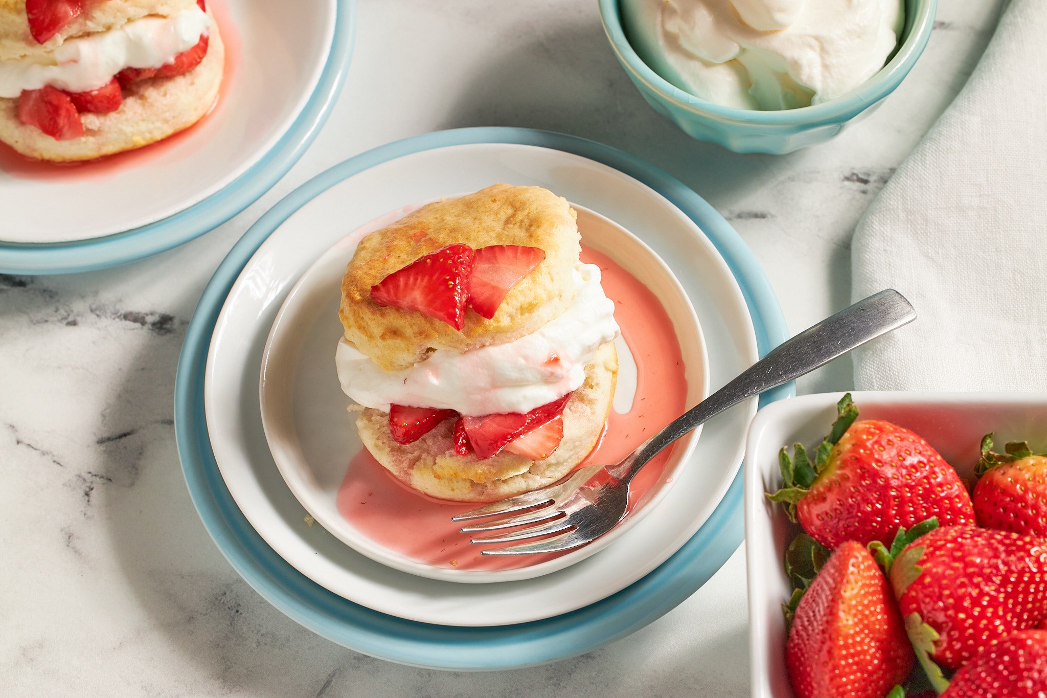 strawberry shortcake with biscuits fresh strawberries and whipped cream on a white plate with a fork on neutral background and aqua dishes
