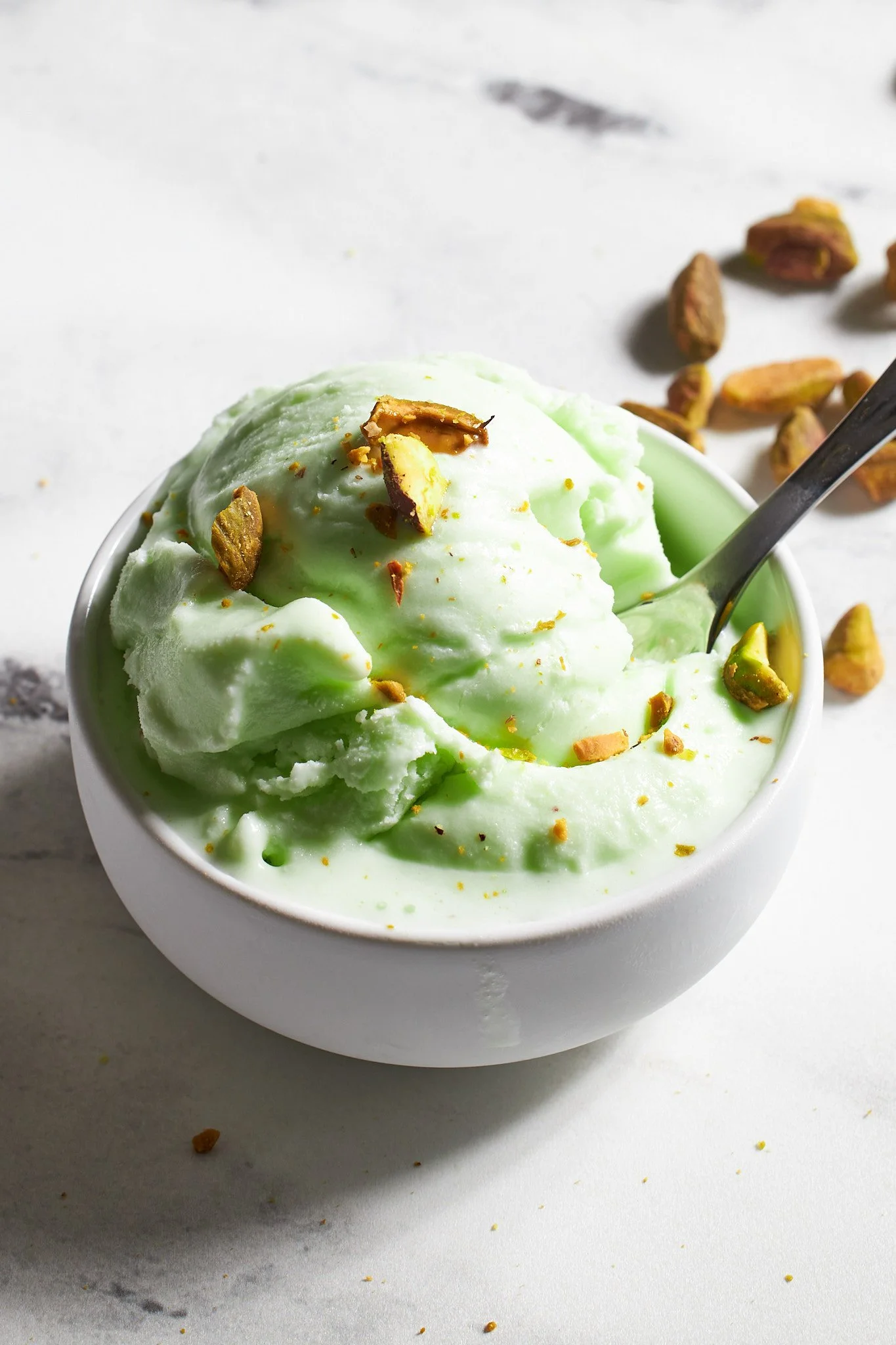 Pistachio ice cream from Ninja Creami in white bowl on neutral surface with pistachios in the background