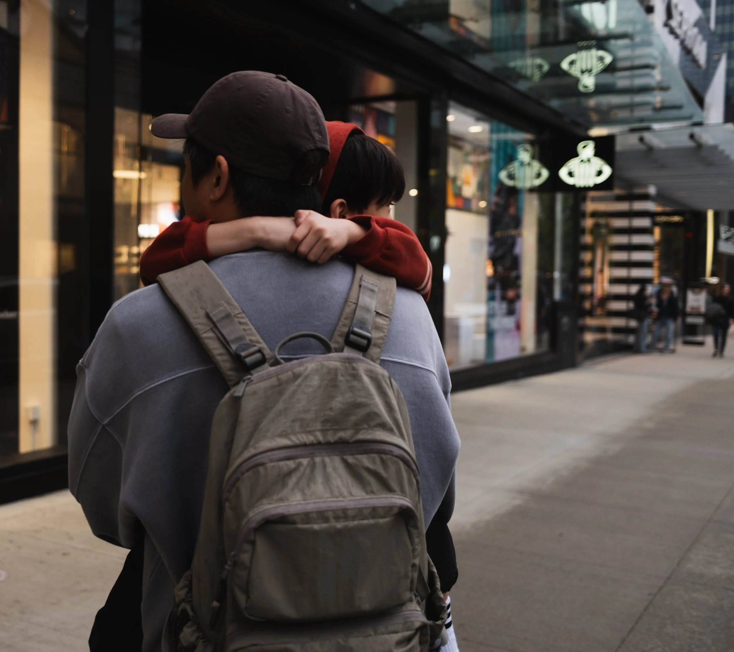 A man carrying a child on his back at an urban transit station.